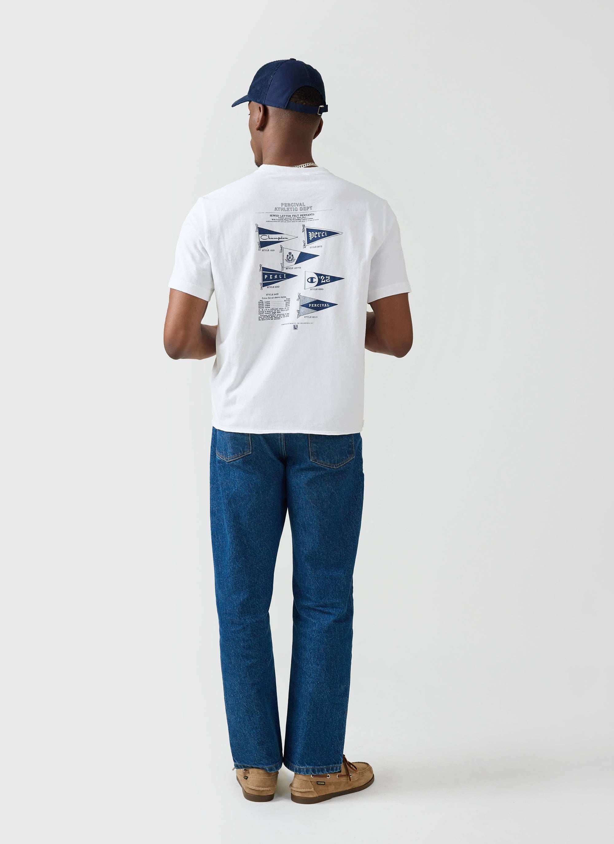 A model from behind wears the white Champion x Percival Flag Raw Hem T-shirt, showcasing the pennant back graphic.