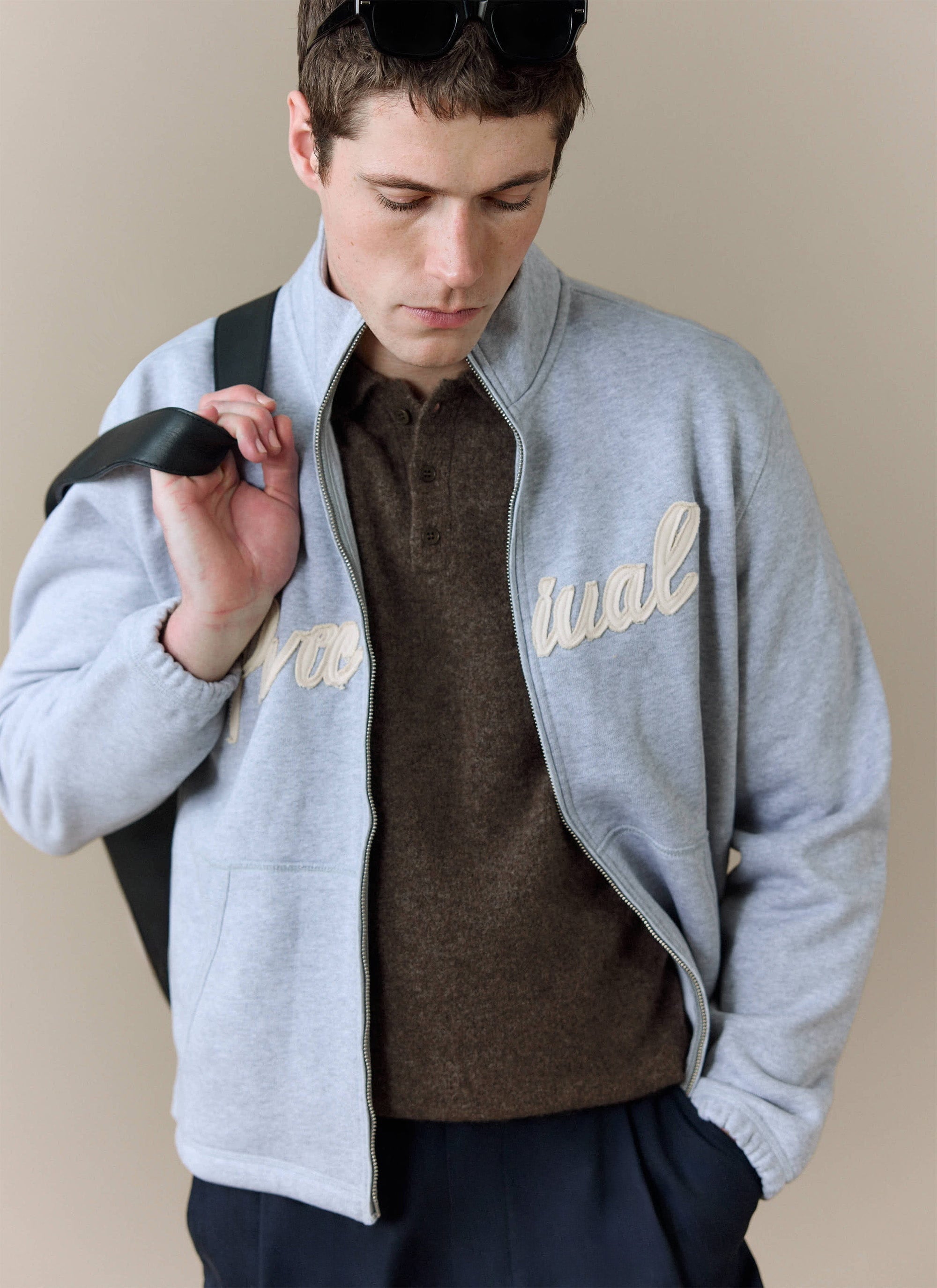 A model wears the espresso Collins Boxy Knitted Polo from Percival, layered under a grey zip-up jacket.