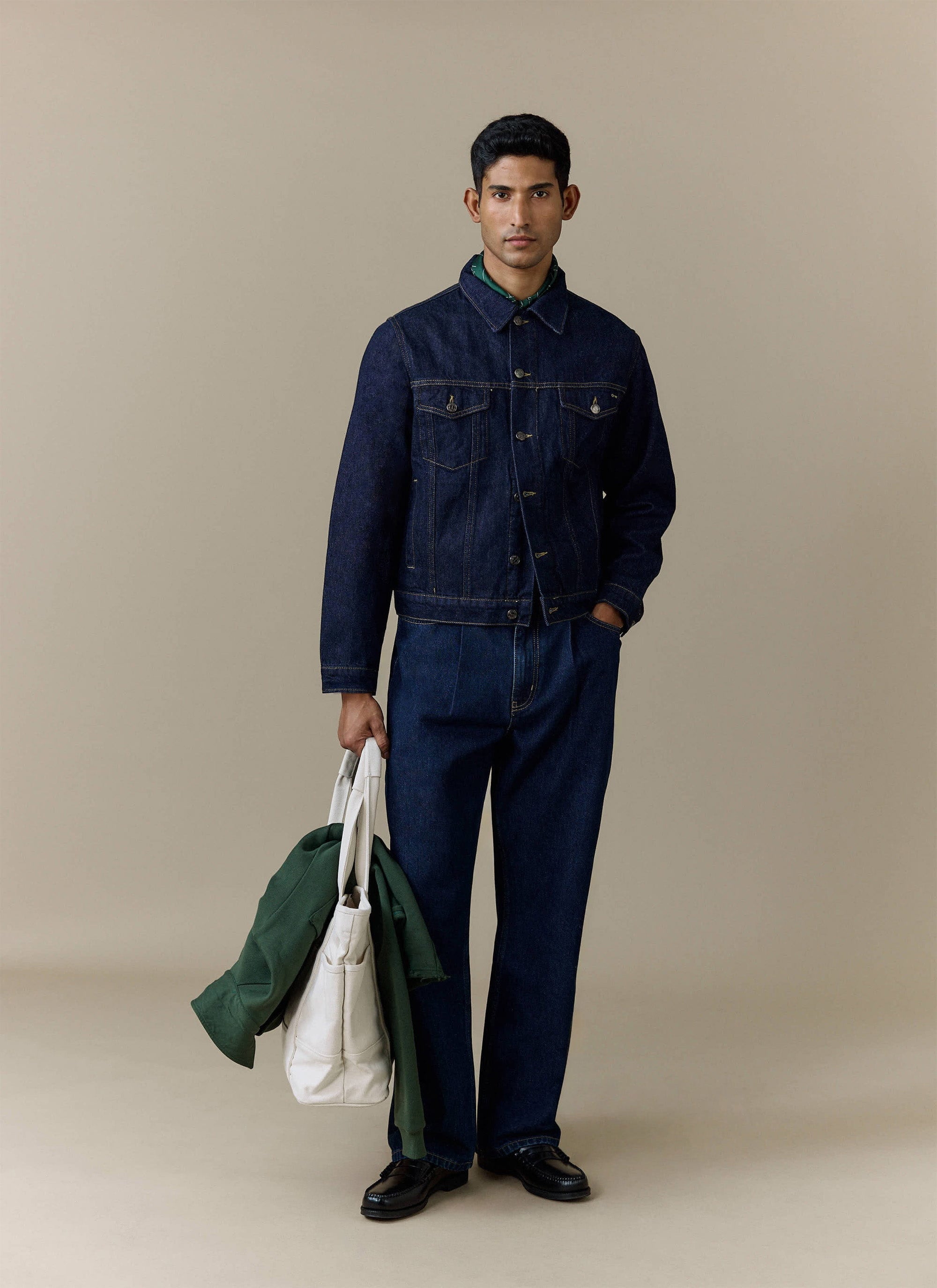 A model wears the Percival Pleated Denim Jeans in dark indigo, styled with a matching denim jacket and black loafers.