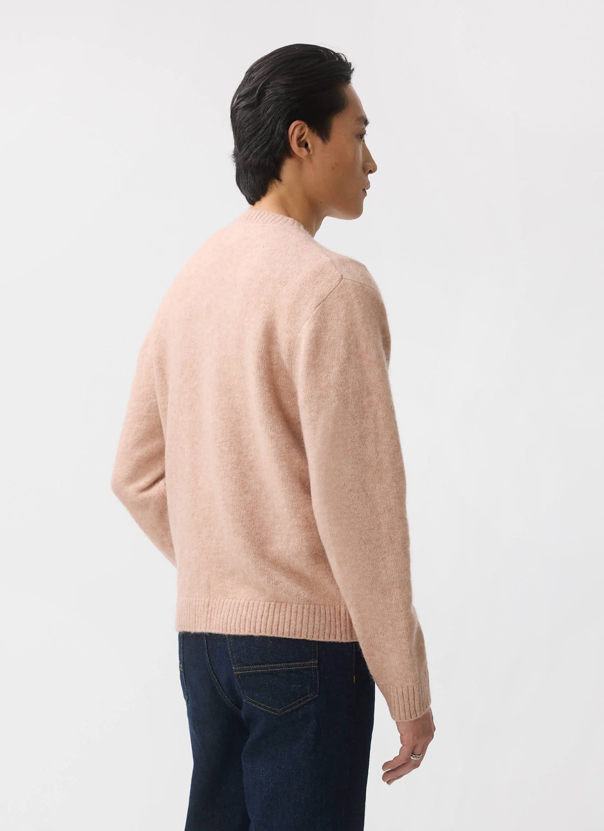 A back-view of a model wearing the Percival White Glove Cardigan in pink, made from a soft wool and mohair blend.