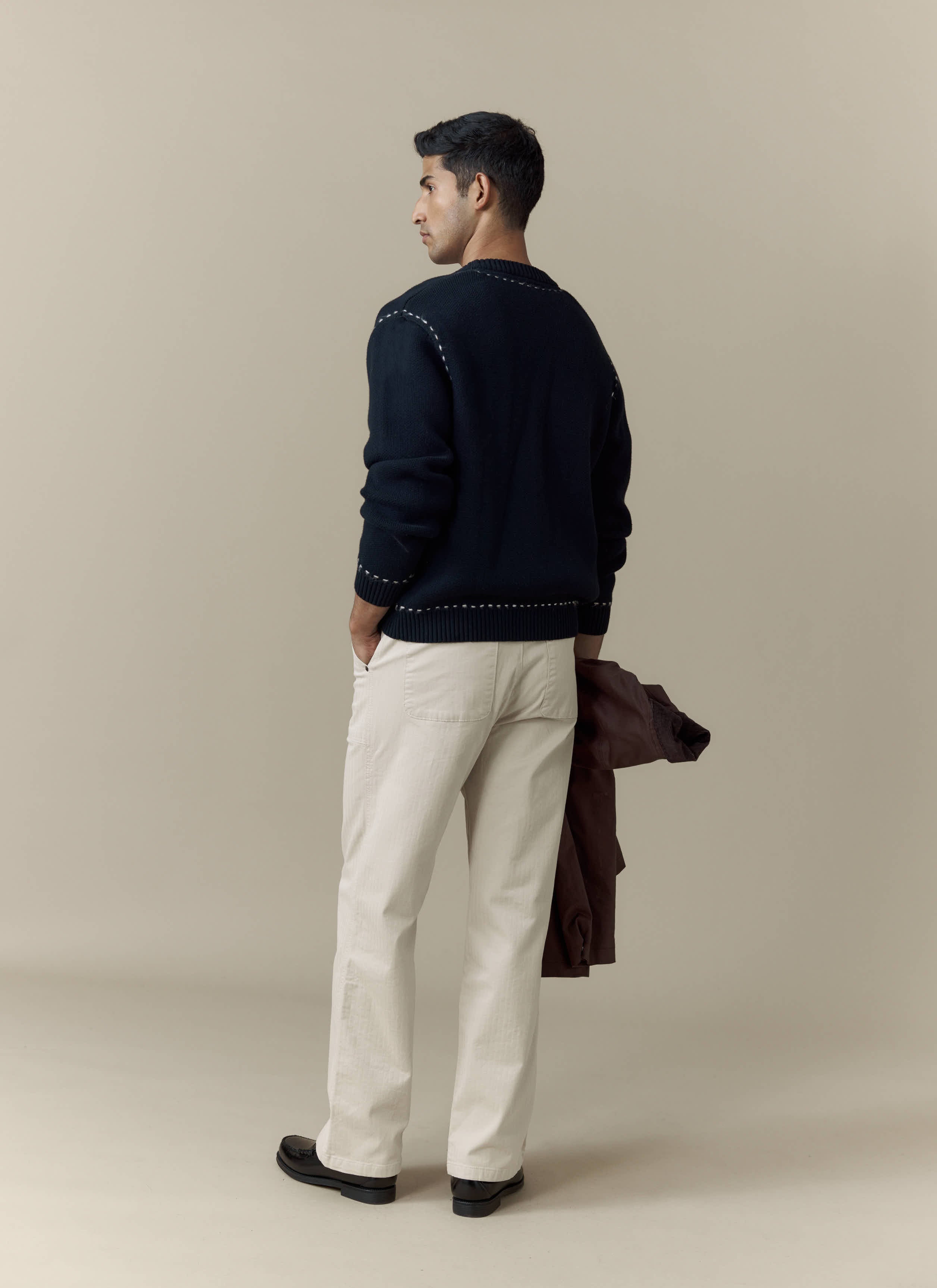 A model wears the Percival Module Boxy Cardigan in black cotton, styled with cream trousers and shot from behind.