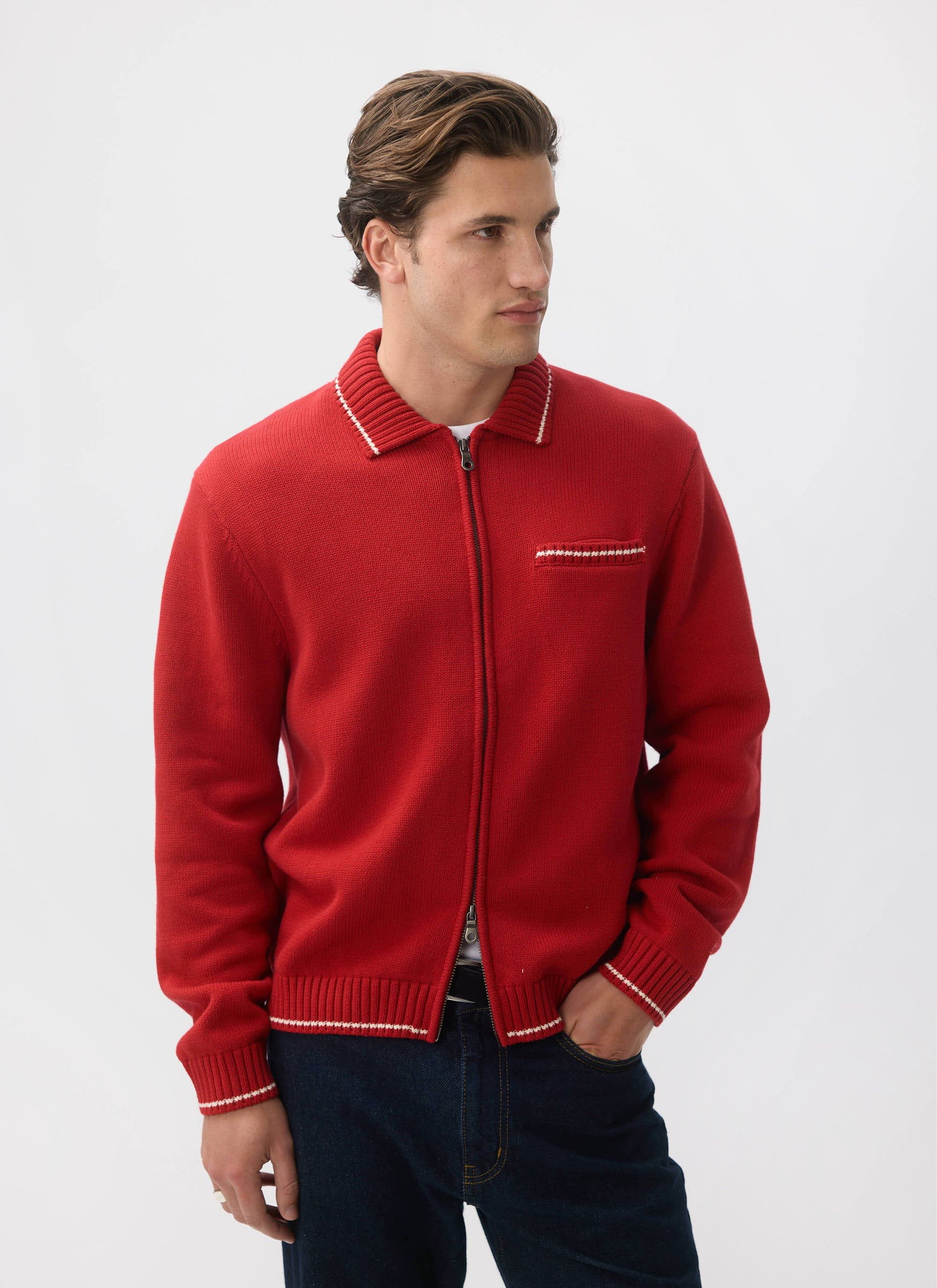 A model wears the Percival Gardner Dense Knitted Zip Cardigan in red, styled with dark blue jeans against a white background.