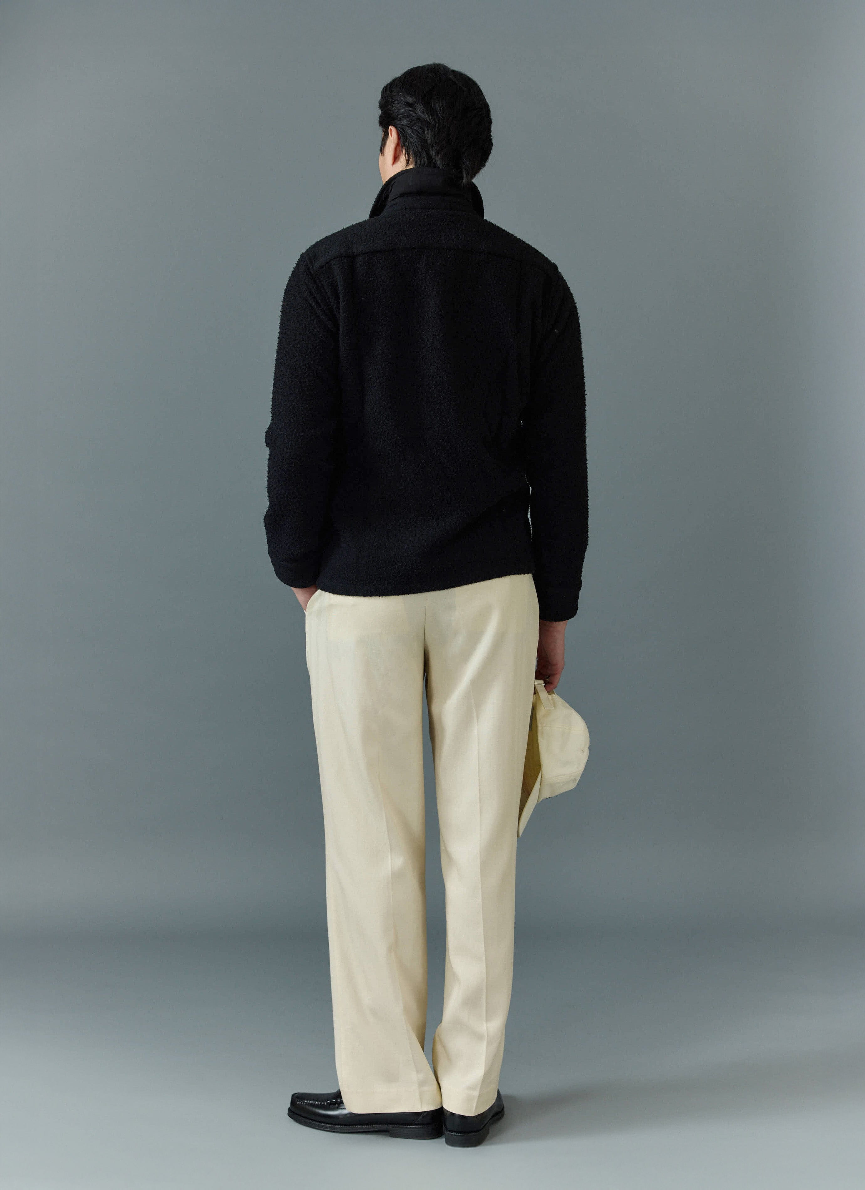 A model wears the black Percival Casentino Wool Blanket Overshirt, pictured from the back with cream trousers.
