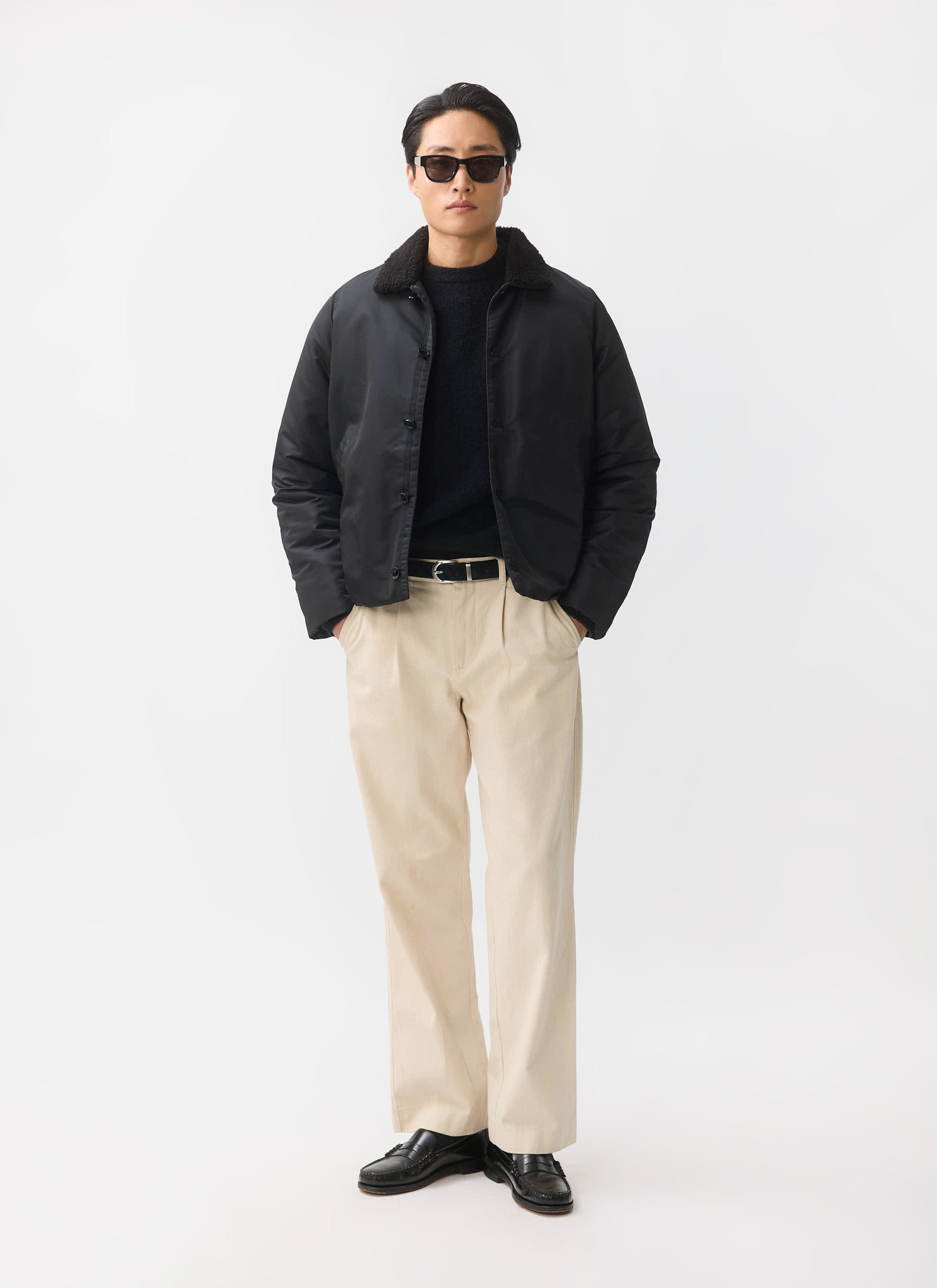 A model styles the black Doppio Bomber Jacket from Percival with a shearling collar, sunglasses and beige trousers.