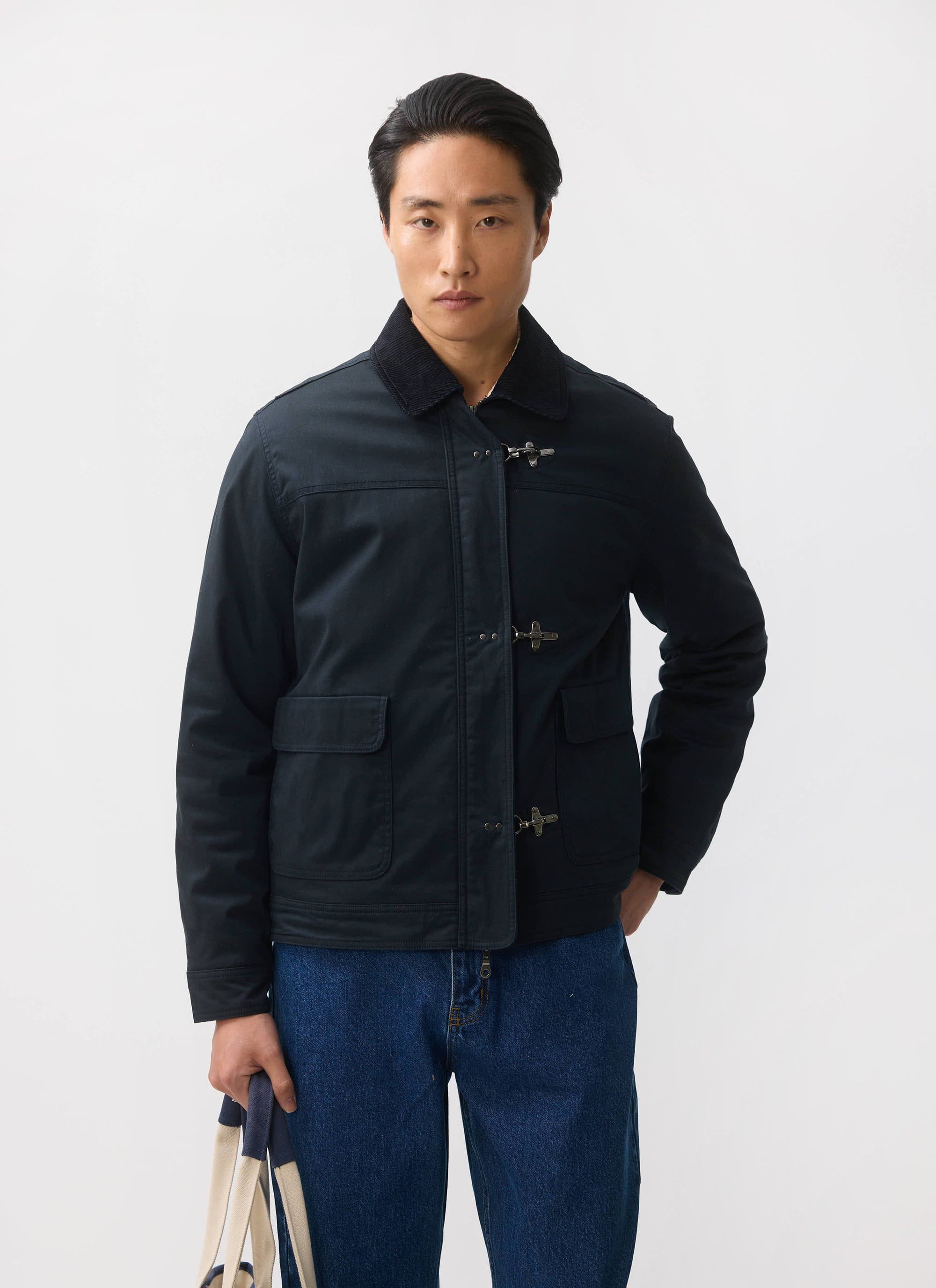 A model wears the navy Percival Fontane Wax Jacket with fireman clasps, paired with blue jeans against a white background.