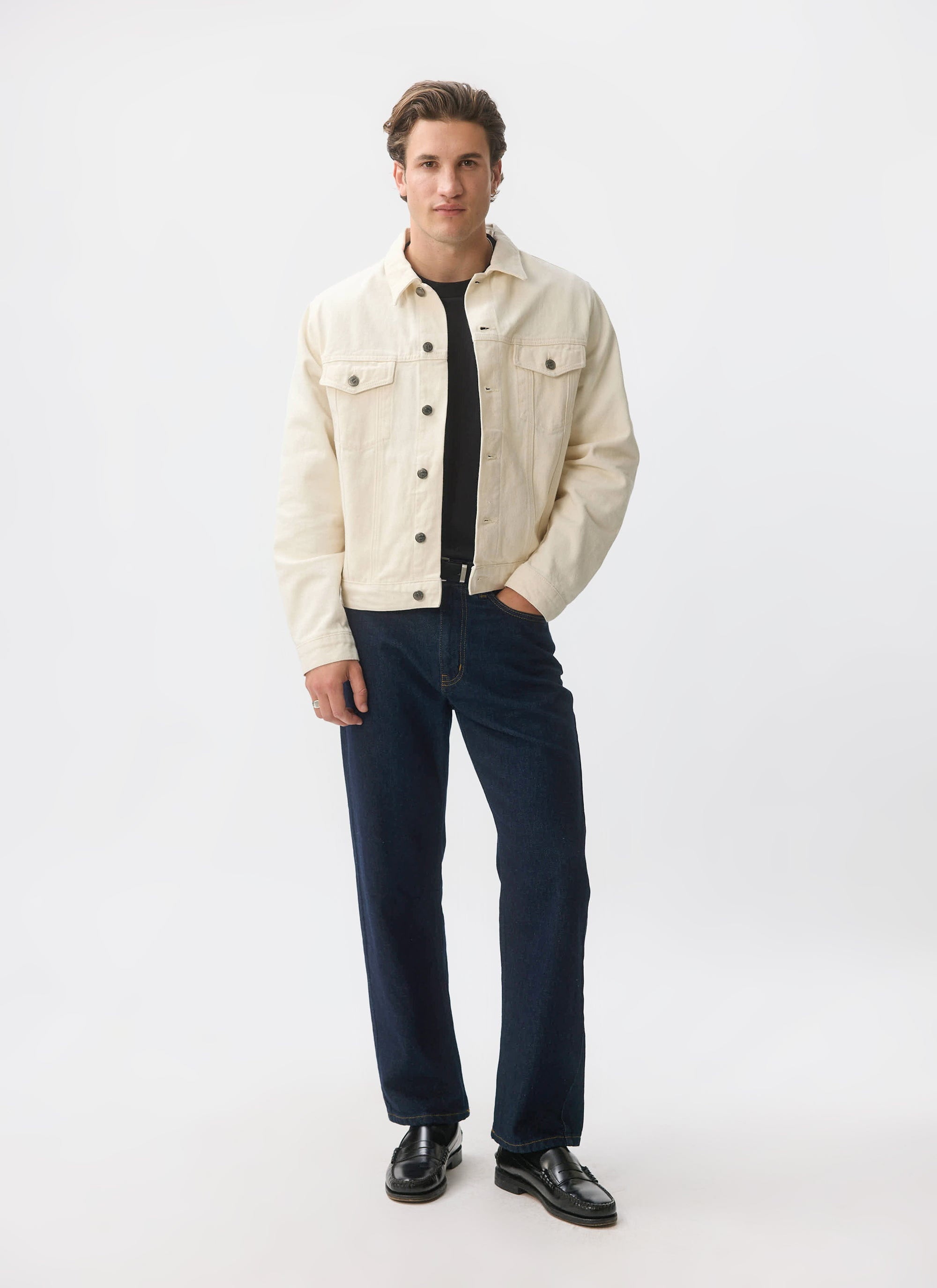 A male model wears the ecru denim Western Trucker Jacket from Percival, paired with dark jeans and a black t-shirt.