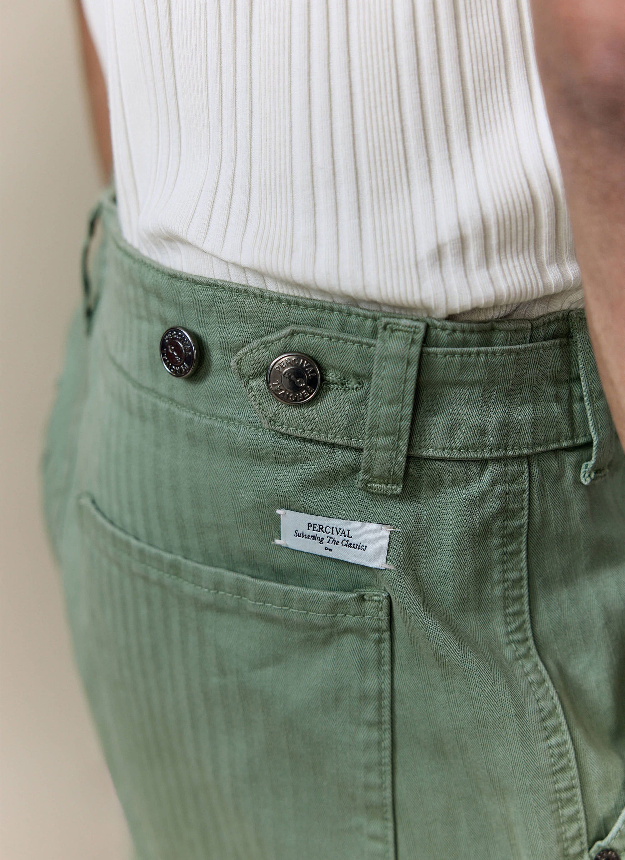 Detailed view of Percival Lungo Herringbone Straight Trousers in sage green cotton, showing the branded buttons and tag.