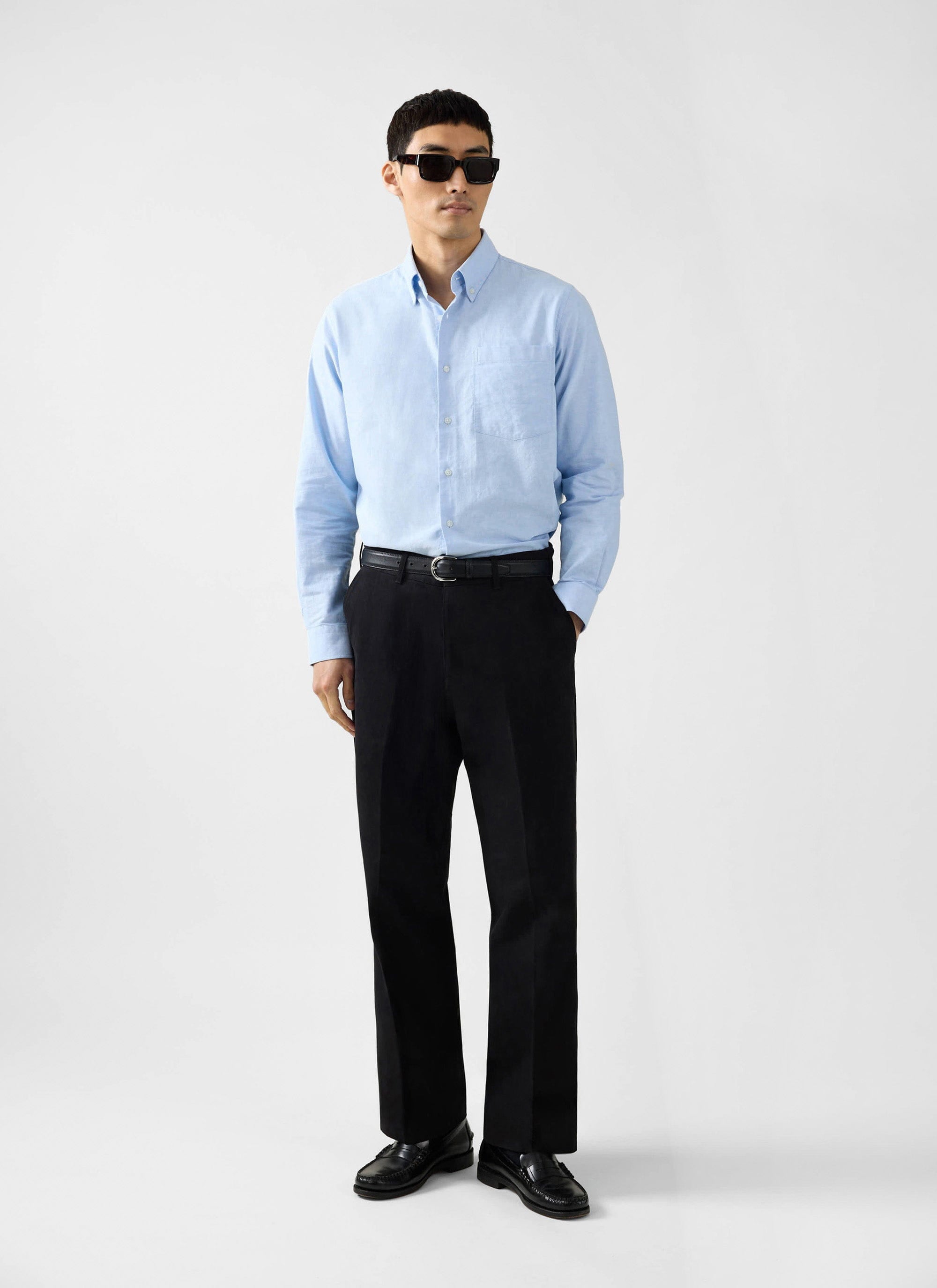 A man models the Percival Oxford Regular Shirt in light blue, paired with smart black trousers and sunglasses.