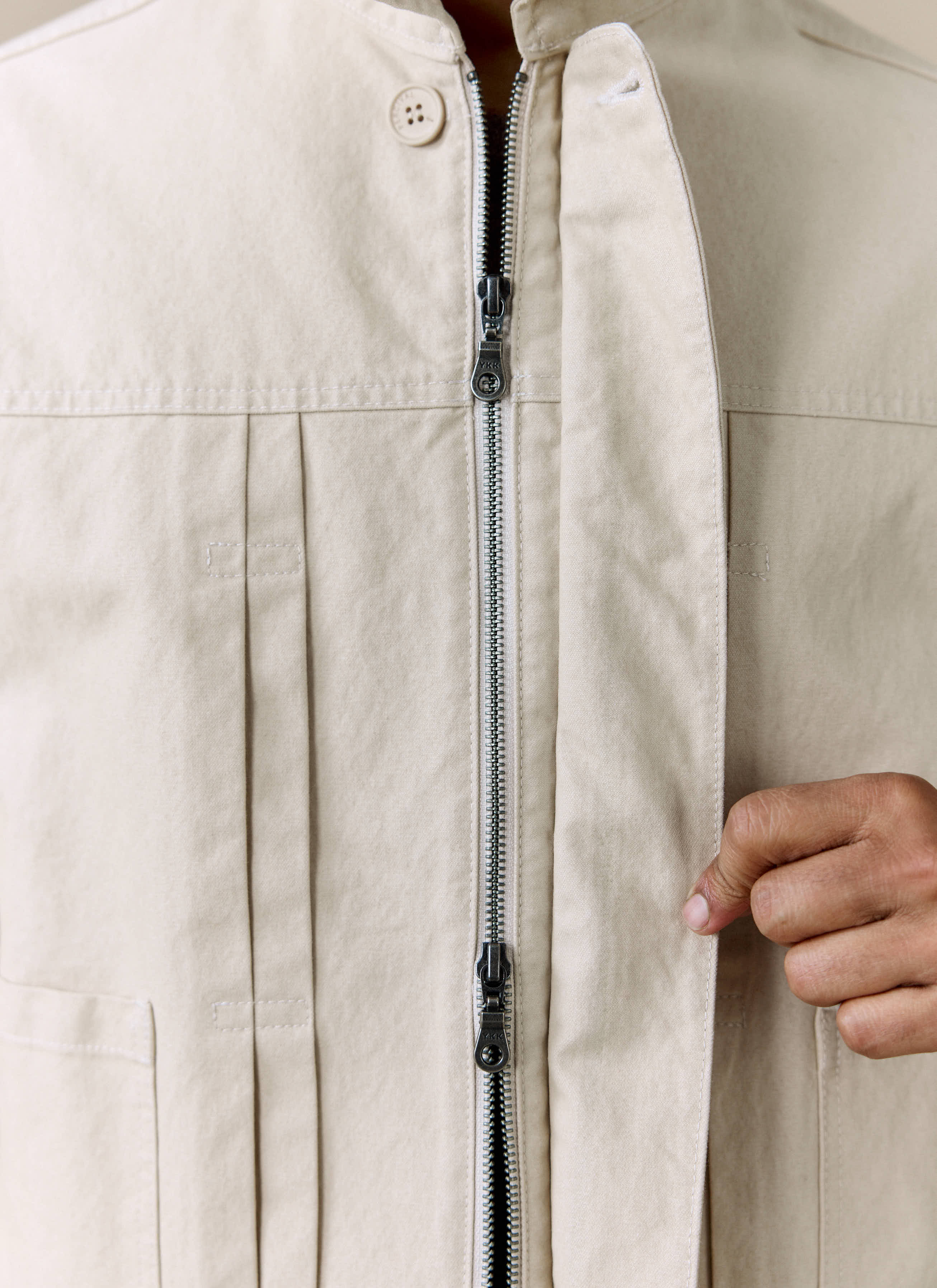 Close-up detail shot of the Percival Ernst Jacket in ecru, showing the two-way zip and twin pleated front.