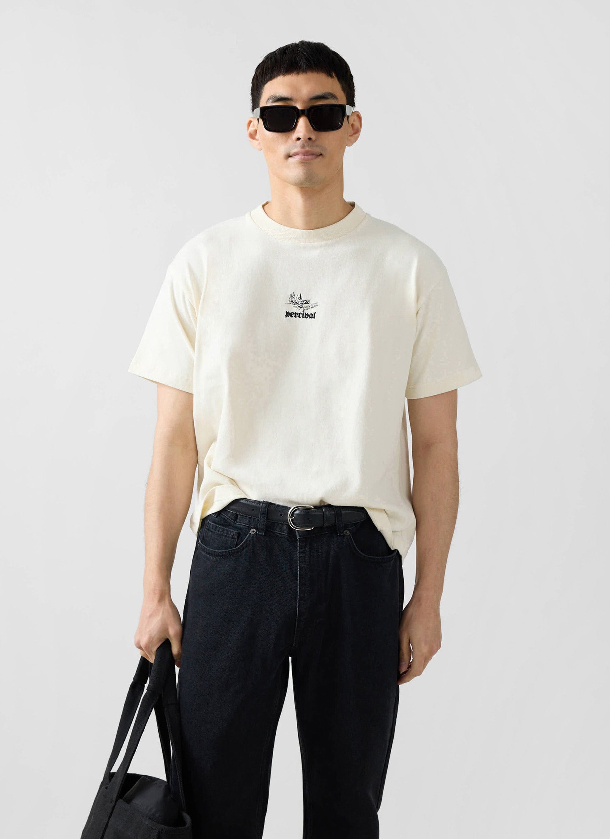 A man models the Percival Wildlands oversized t-shirt in ecru, styled with black jeans and sunglasses.