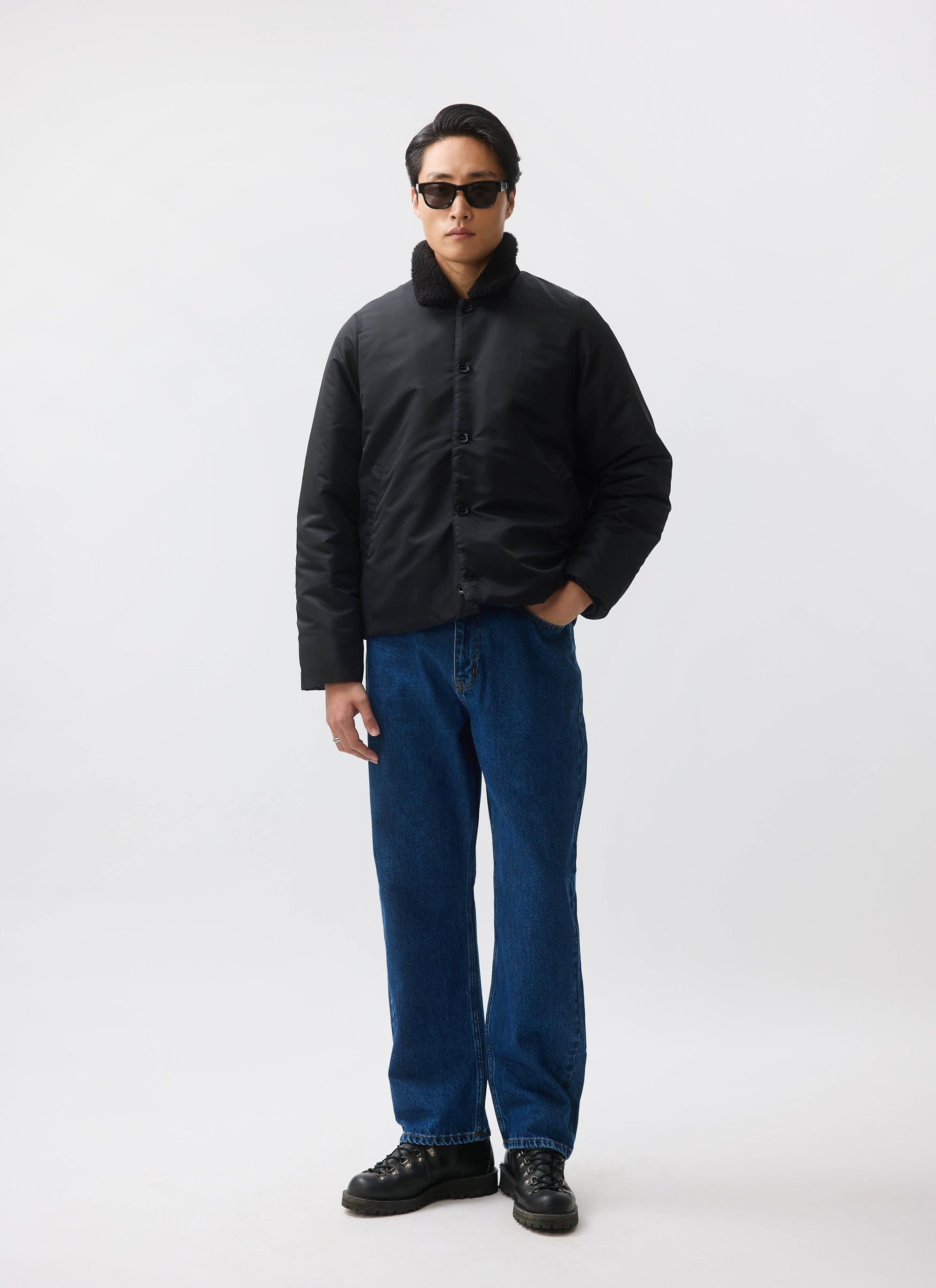 A model wears the black nylon Doppio Bomber Jacket from Percival, featuring a faux shearling collar, styled with blue jeans.