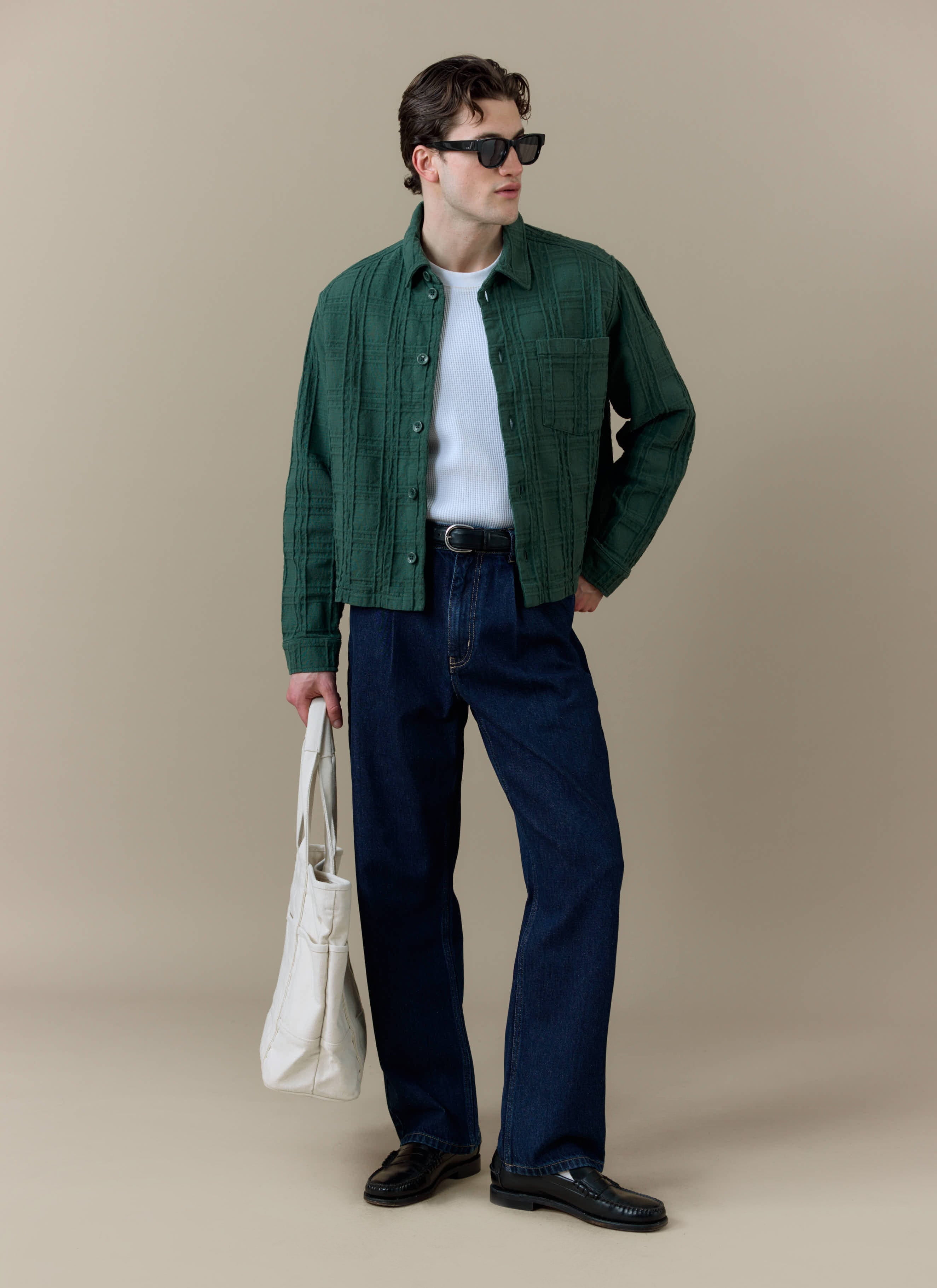 A model wearing the Percival Canyon Heavyweight Overshirt in forest green, styled with dark trousers and a white tote bag.