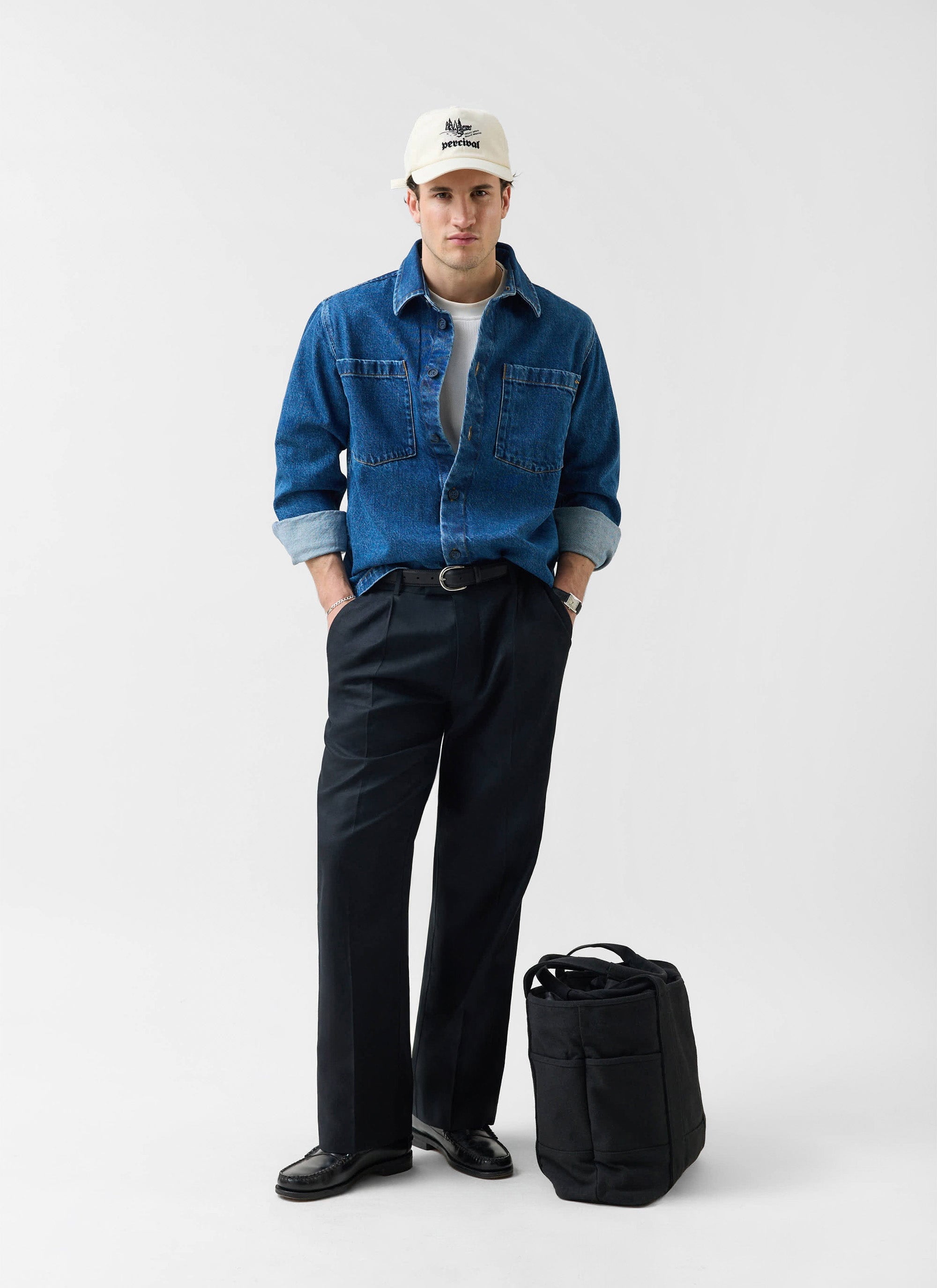 A model wears the Percival Denim Heavyweight Overshirt in mid-wash blue, styled with dark trousers and a Percival cap.
