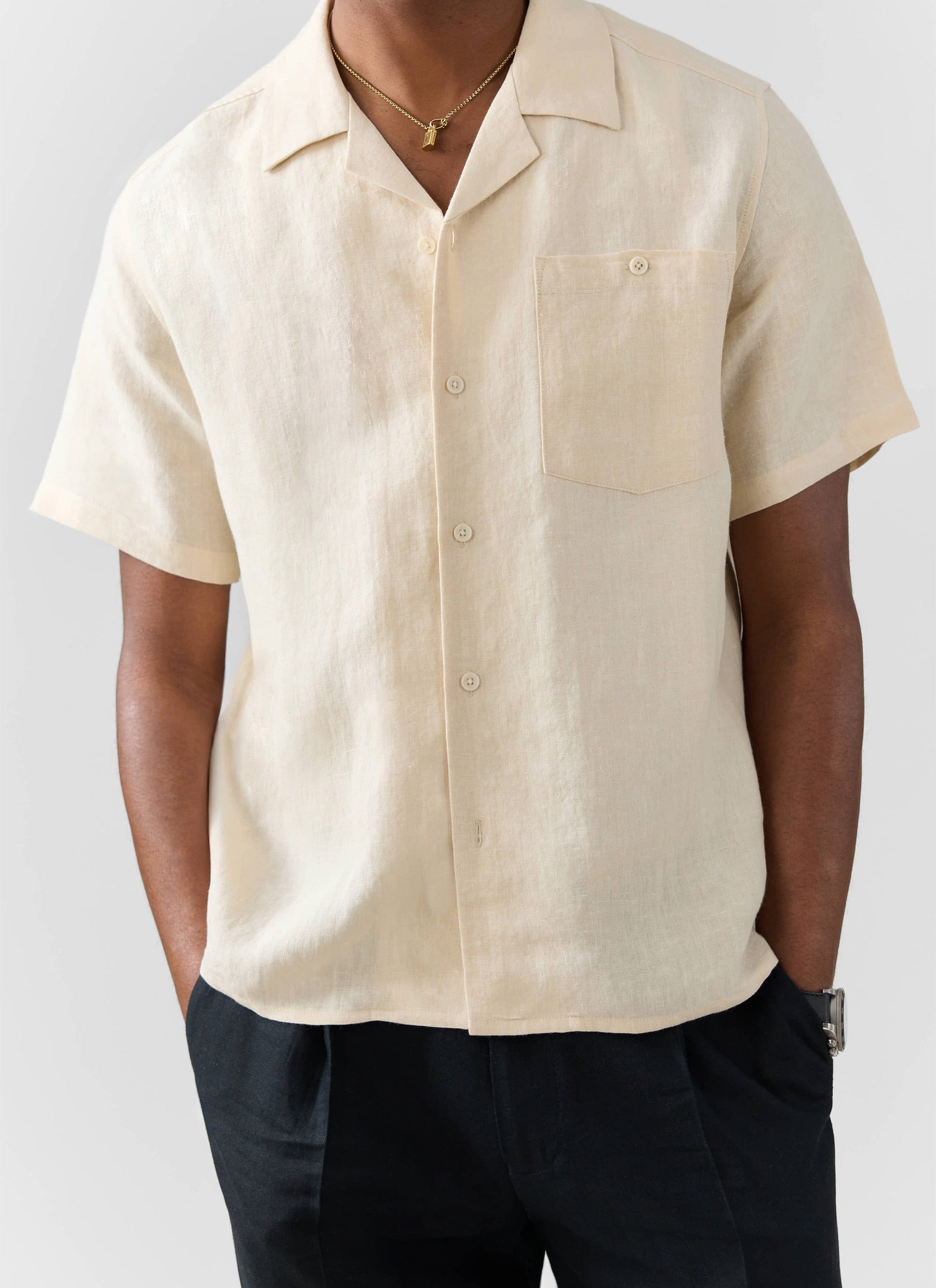A model wears the Percival Short Sleeve Cuban Shirt in cream linen, styled with black trousers.