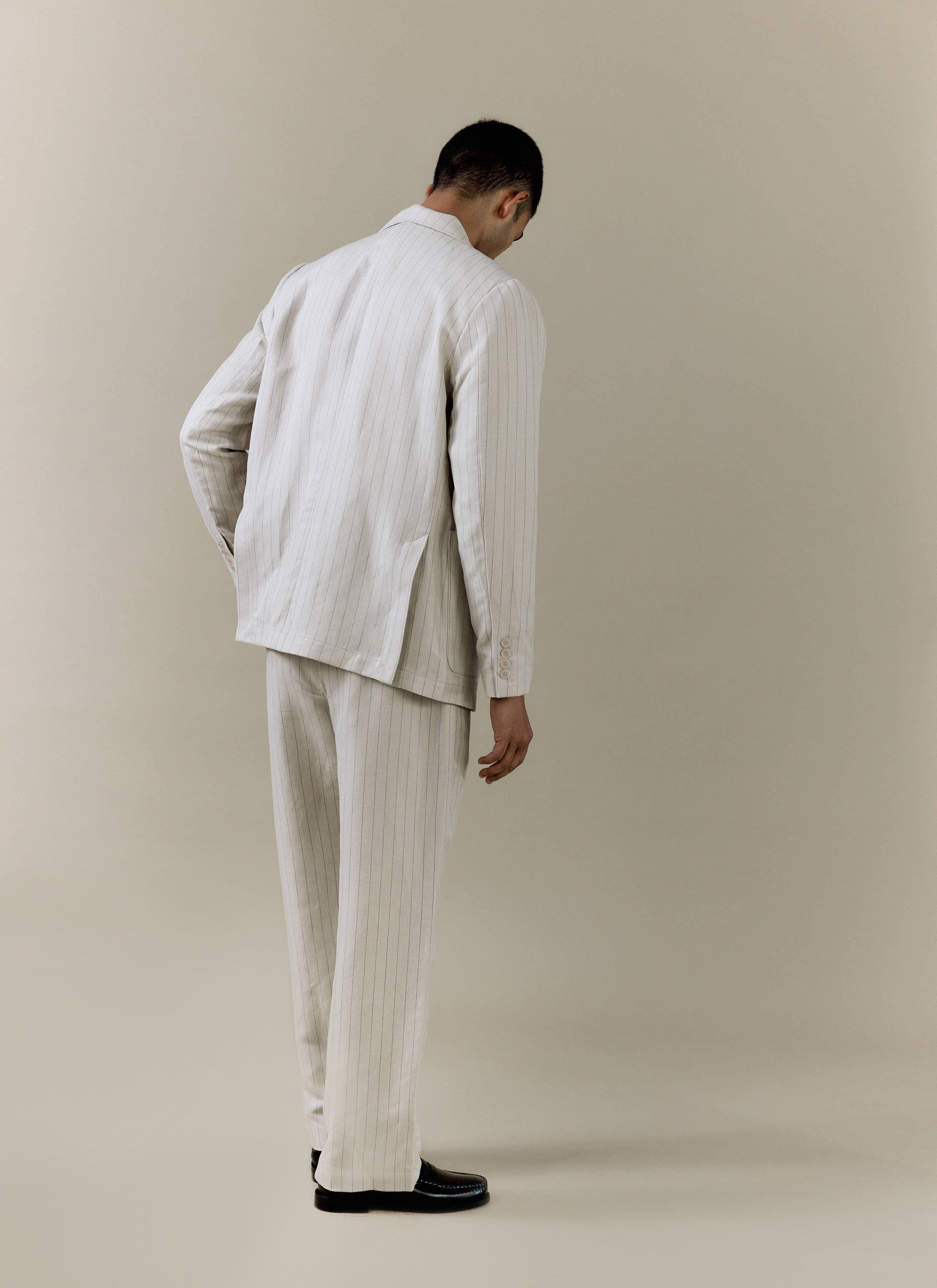 A rear view of a model wearing the cream striped tailored blazer and matching trousers from Percival.