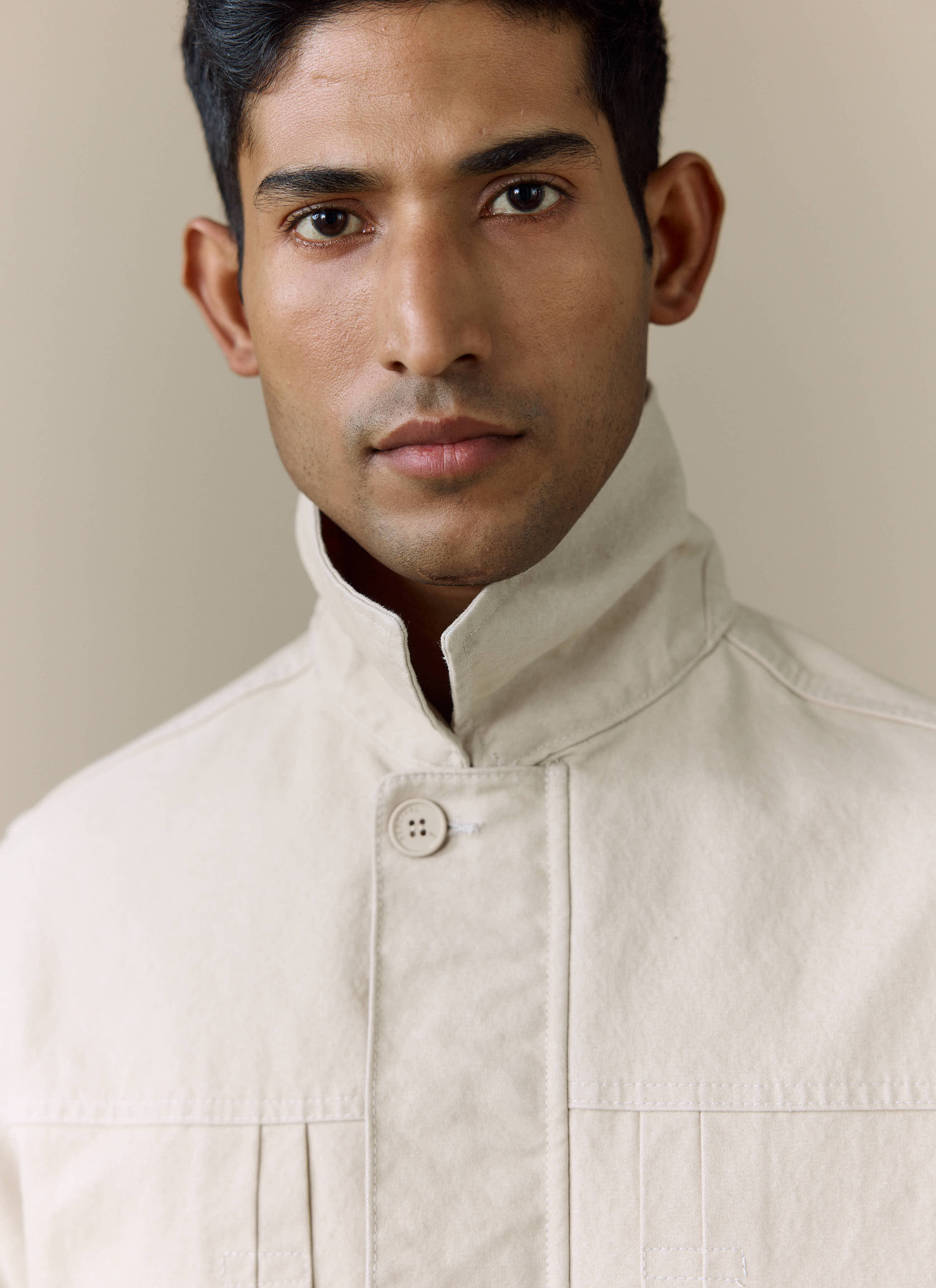A close-up of a model wearing the Percival Ernst Jacket in ecru, showing the popped collar and button detail.