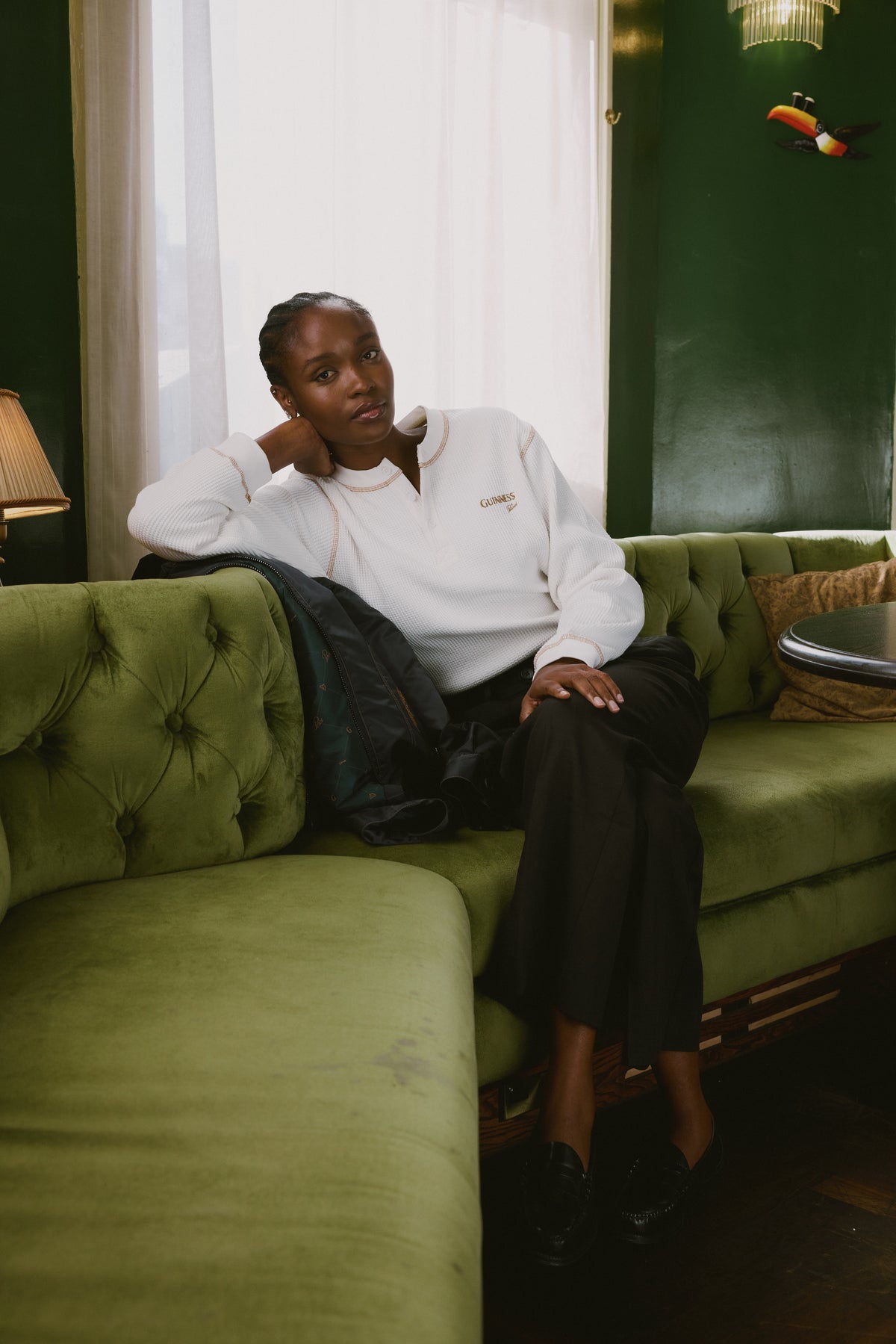 Model wearing the cream Guinness x Percival waffle henley long sleeve t-shirt while relaxing on a green velvet sofa.