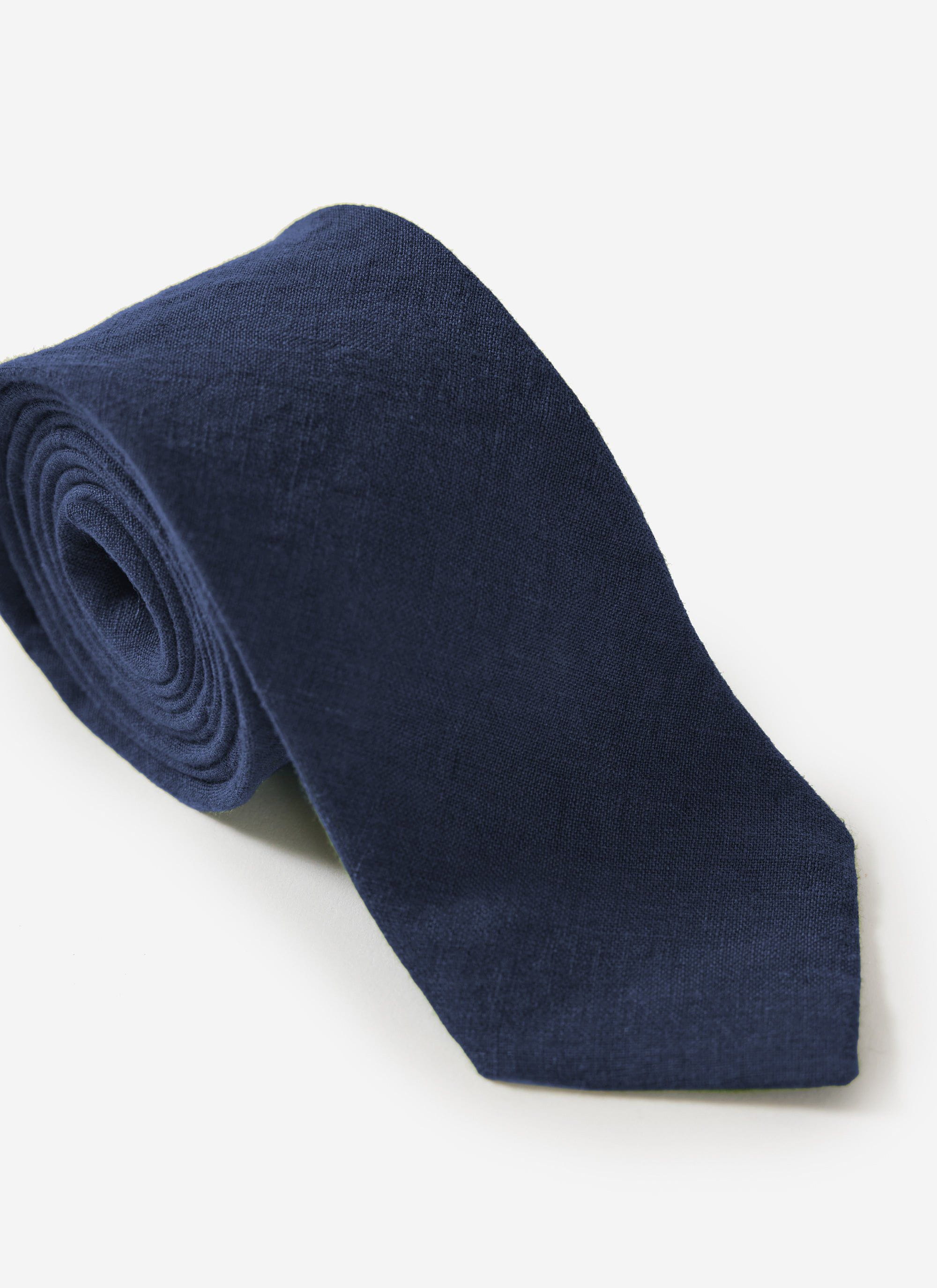 A close-up of the Percival Linen Tie in navy, rolled neatly against a plain white background to highlight its texture.