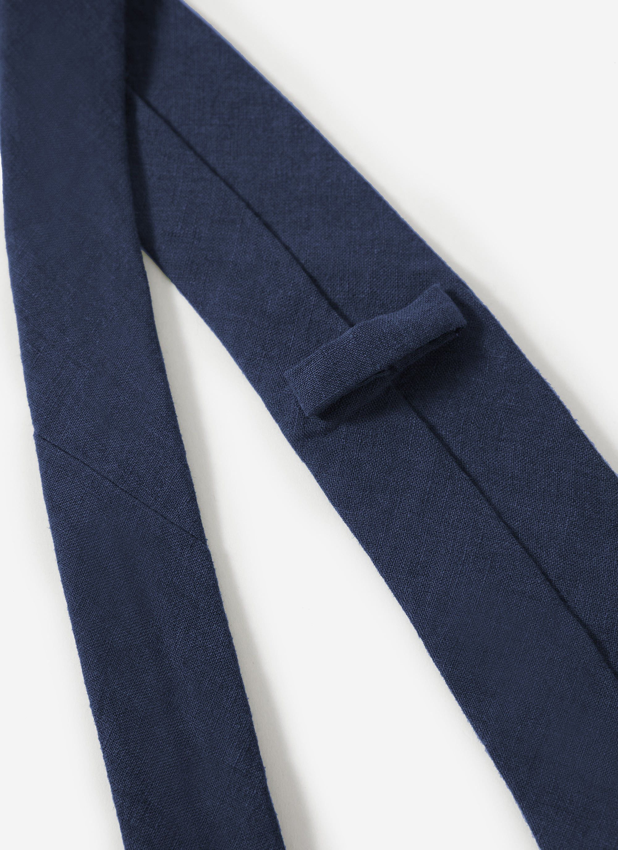 A close-up shot of the Percival Linen Tie in navy, showing the textured fabric and keeper loop detail.