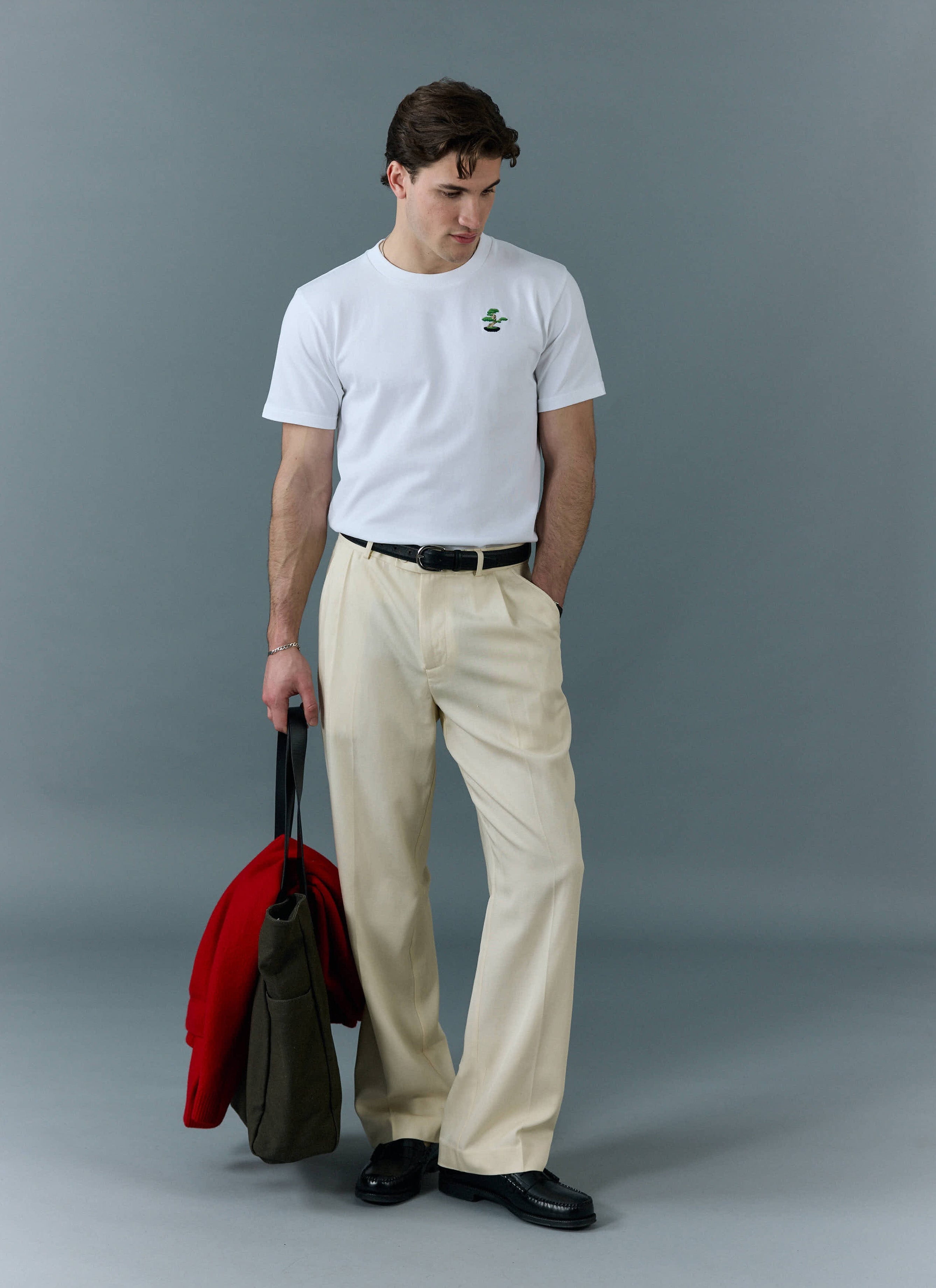 A man models the white Percival Bonsai T-shirt, styled with cream trousers and black loafers in a studio.