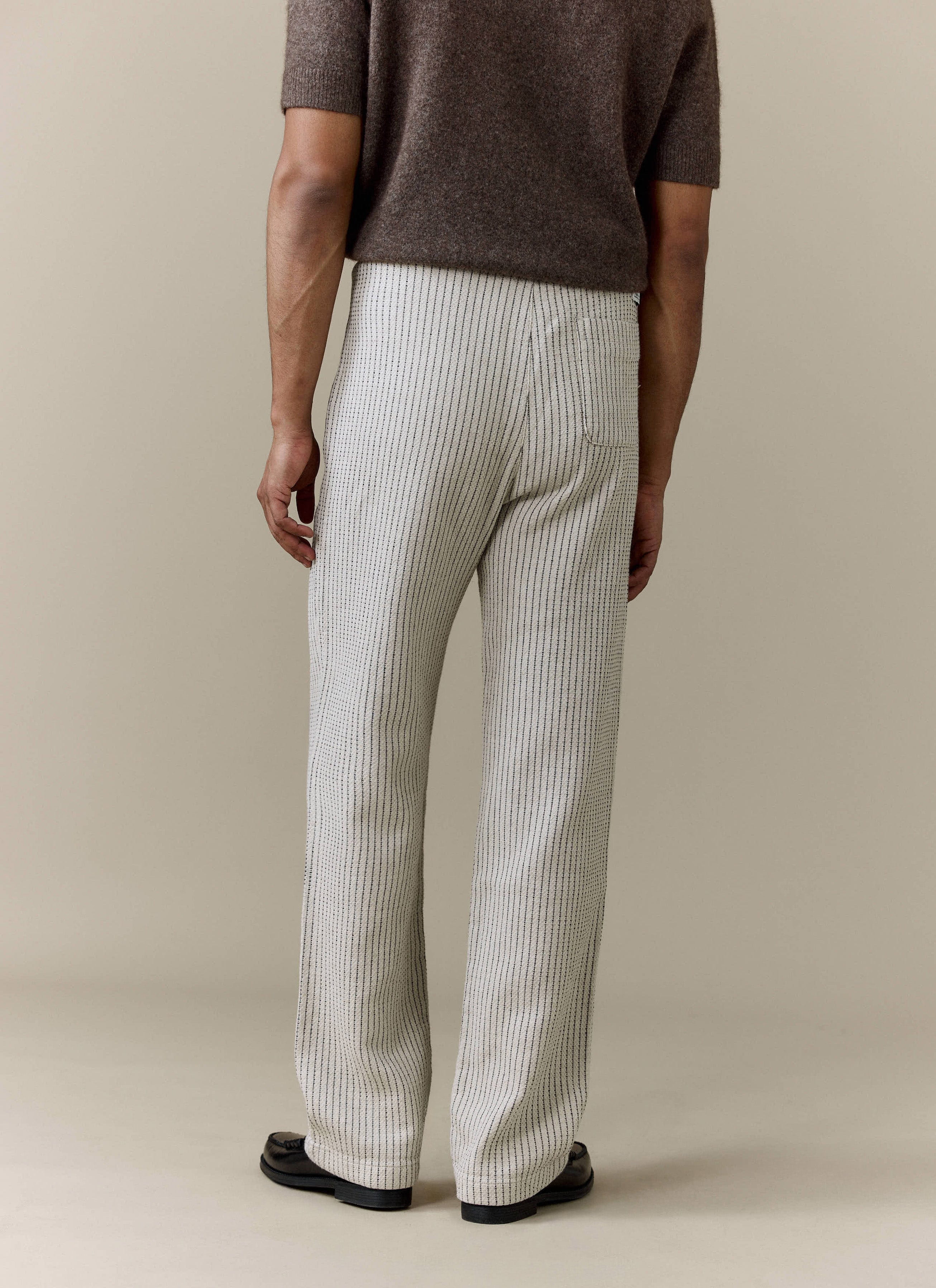 A rear view of a model wearing the ecru linen Sorrento Wide Leg Trousers from Percival, showing off the relaxed fit.