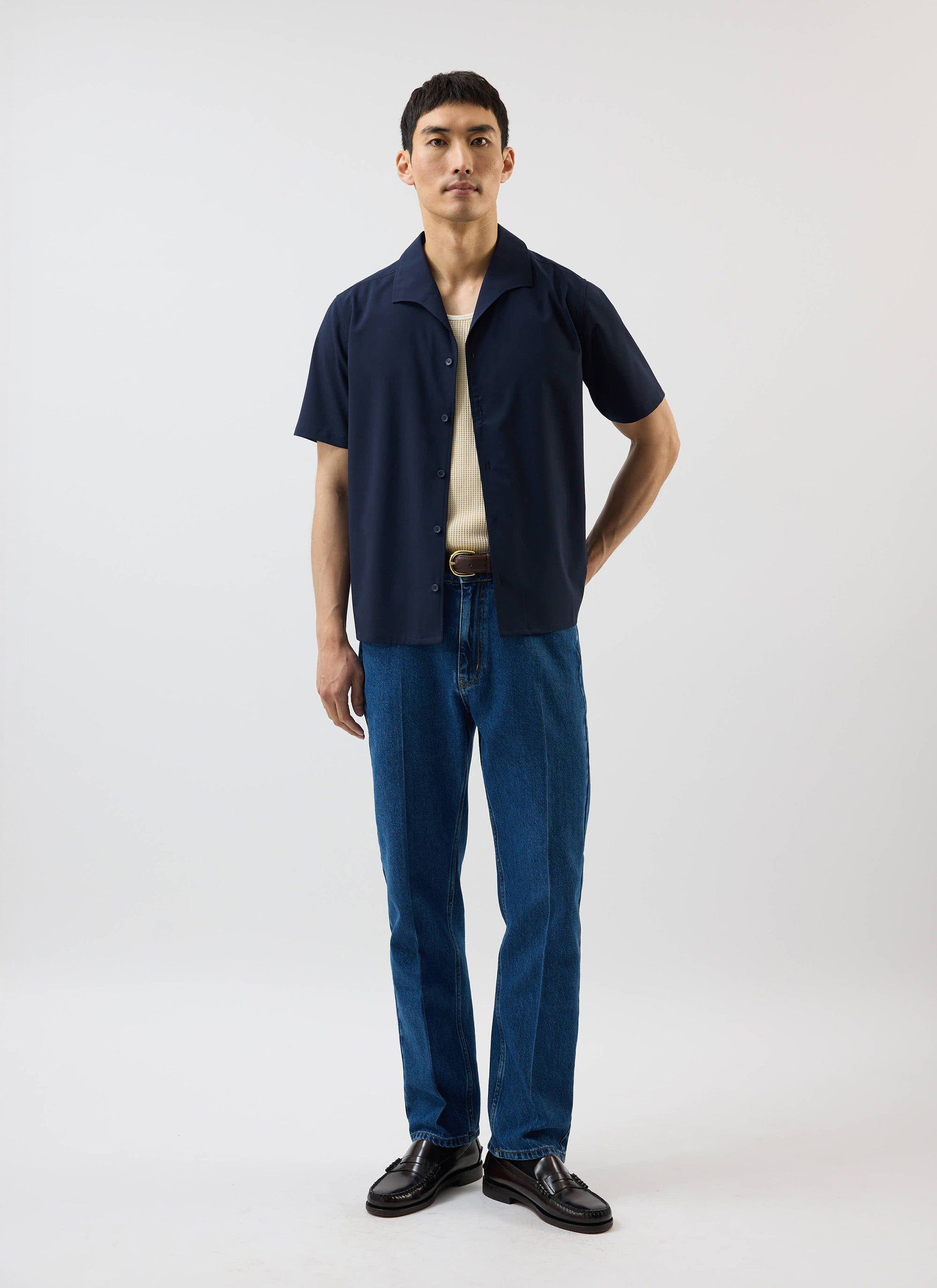 A model wears the Percival x Warren Relaxed Cuban Drape Shirt in navy blue, styled open over a cream vest with blue jeans.