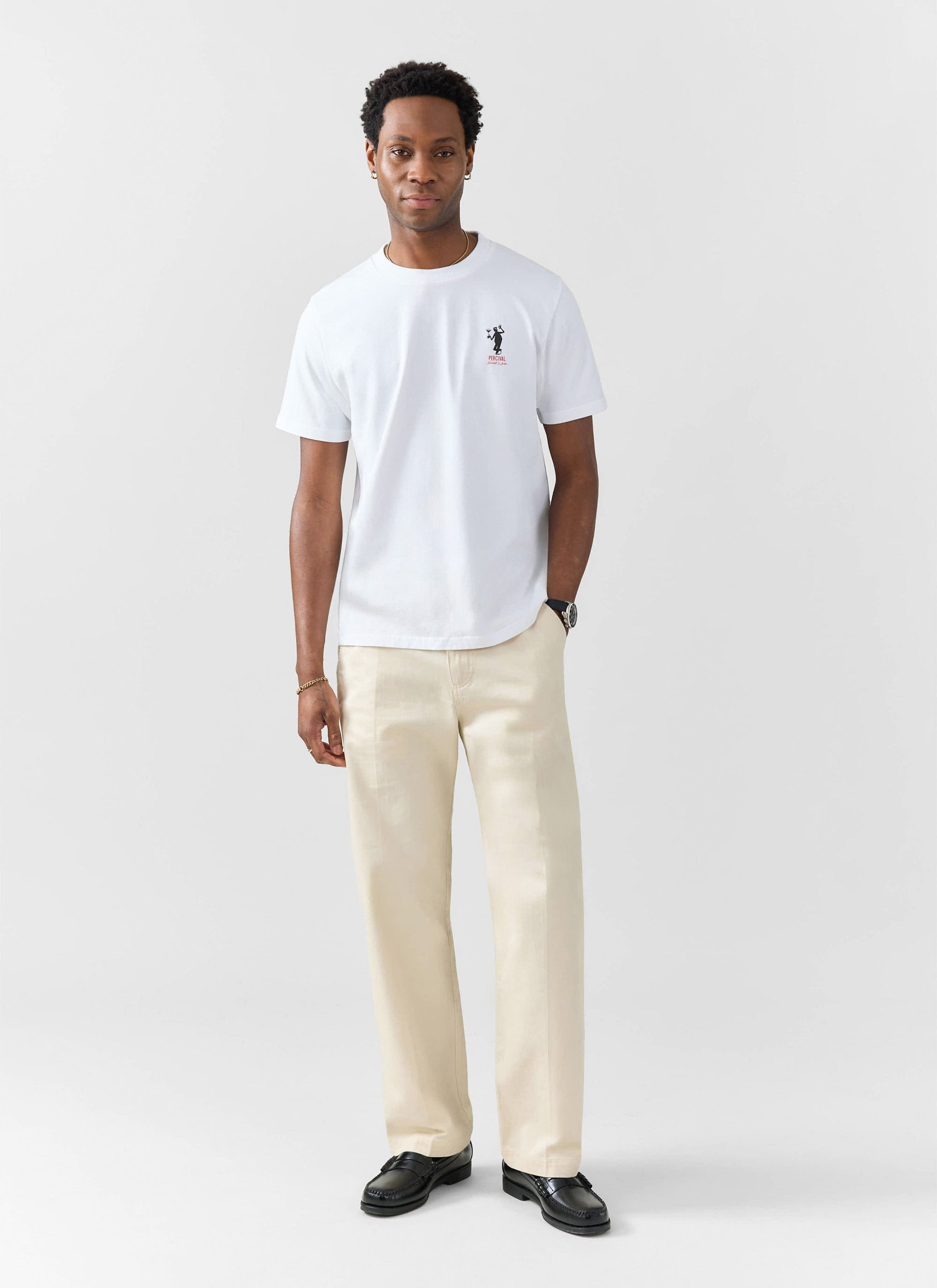 A model wears the Percival Carlo Mixologist T-Shirt in white, paired with cream trousers and black loafers.