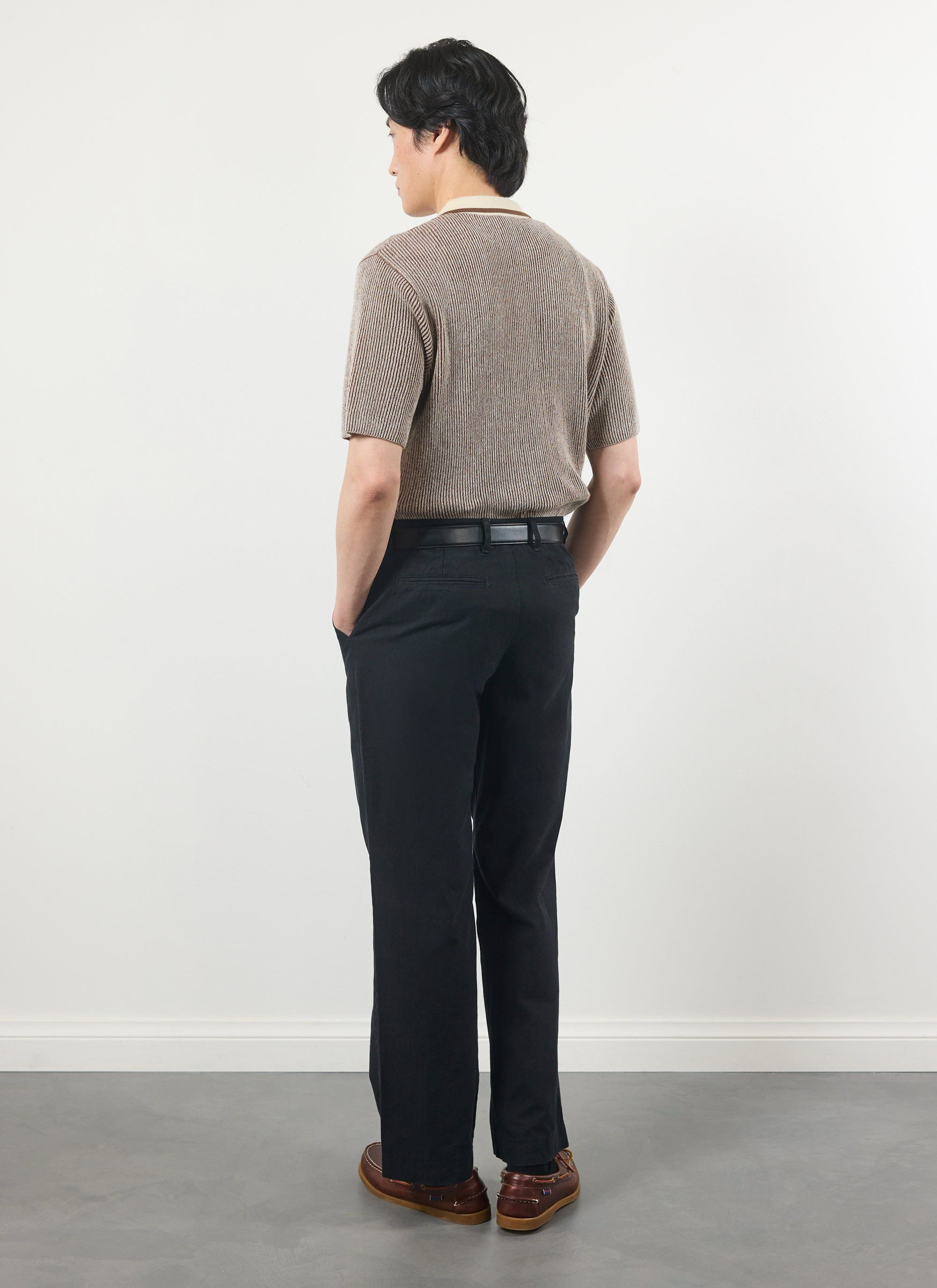 A male model seen from the back wearing the Percival Teramo Knitted Polo in ecru, paired with smart black trousers.