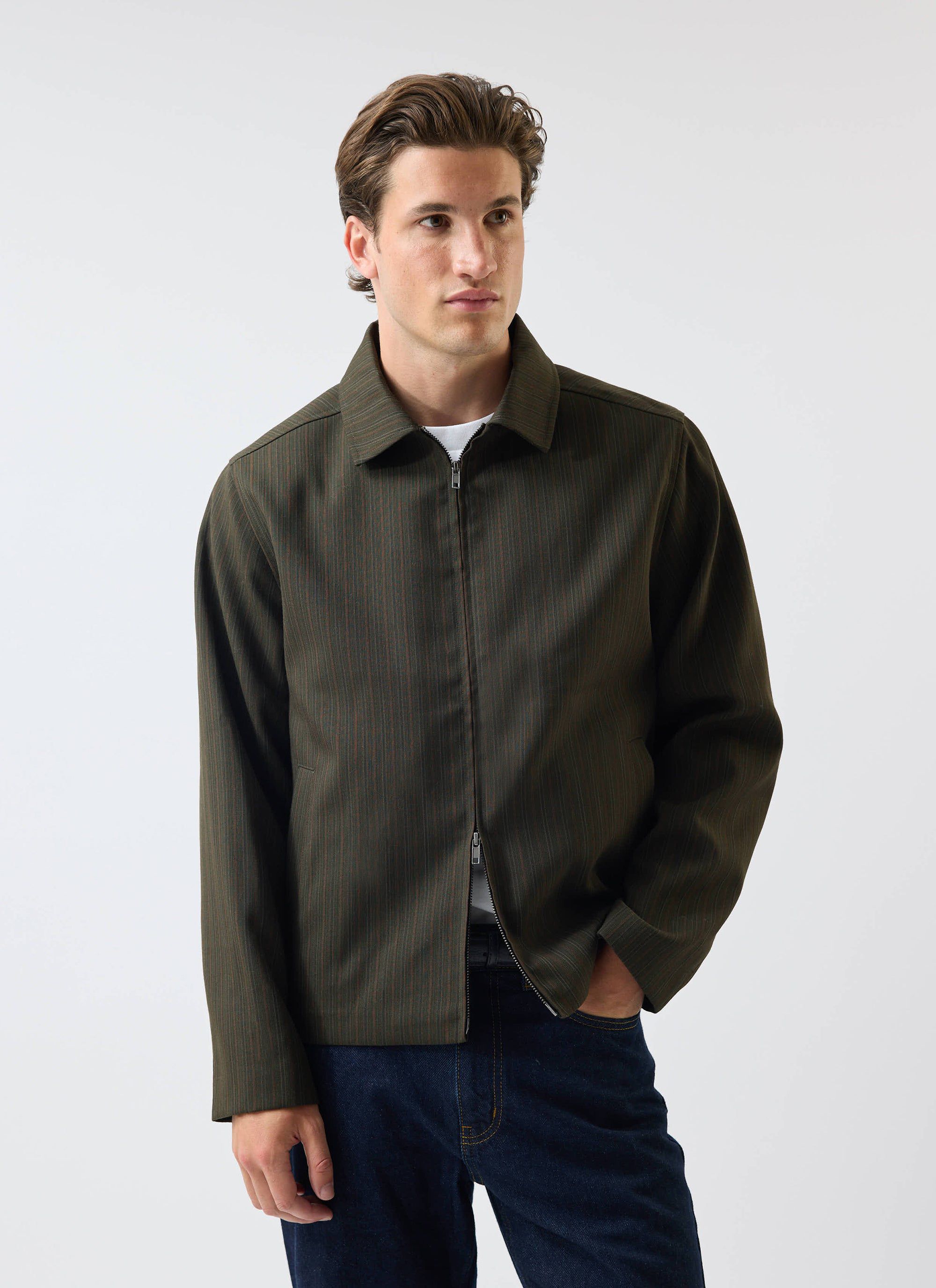 A model wears the Percival Chapter Zip Up Jacket in forest green, styled with a white t-shirt and dark blue jeans.