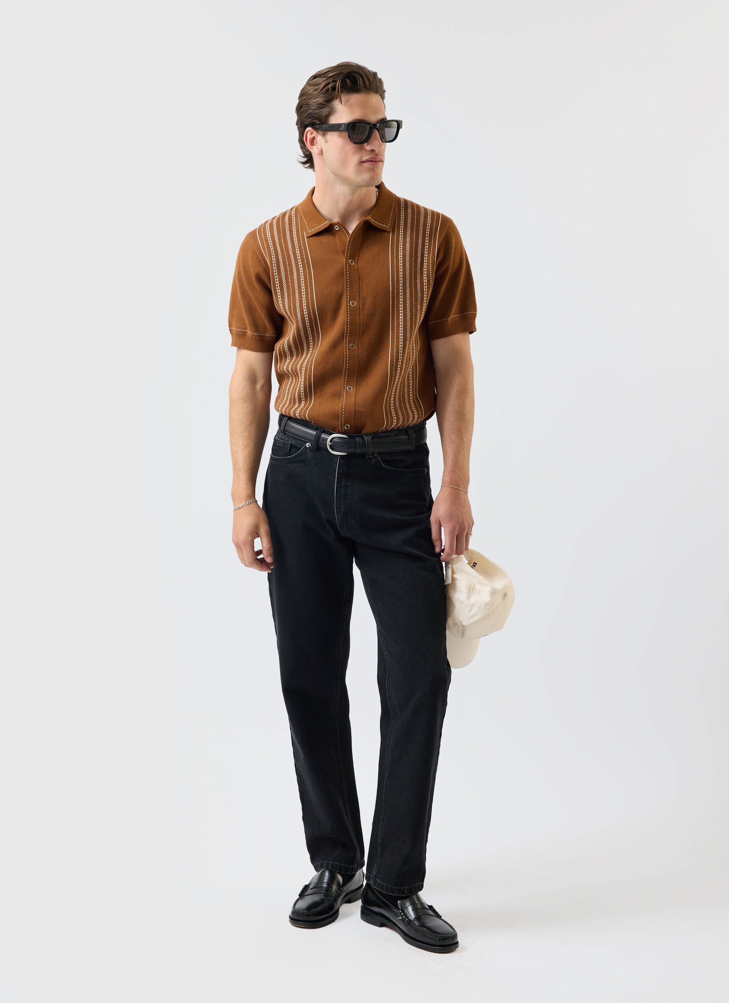 A model wears the Percival Accolades Knitted Shirt in tobacco brown, styled with black jeans and sunglasses.