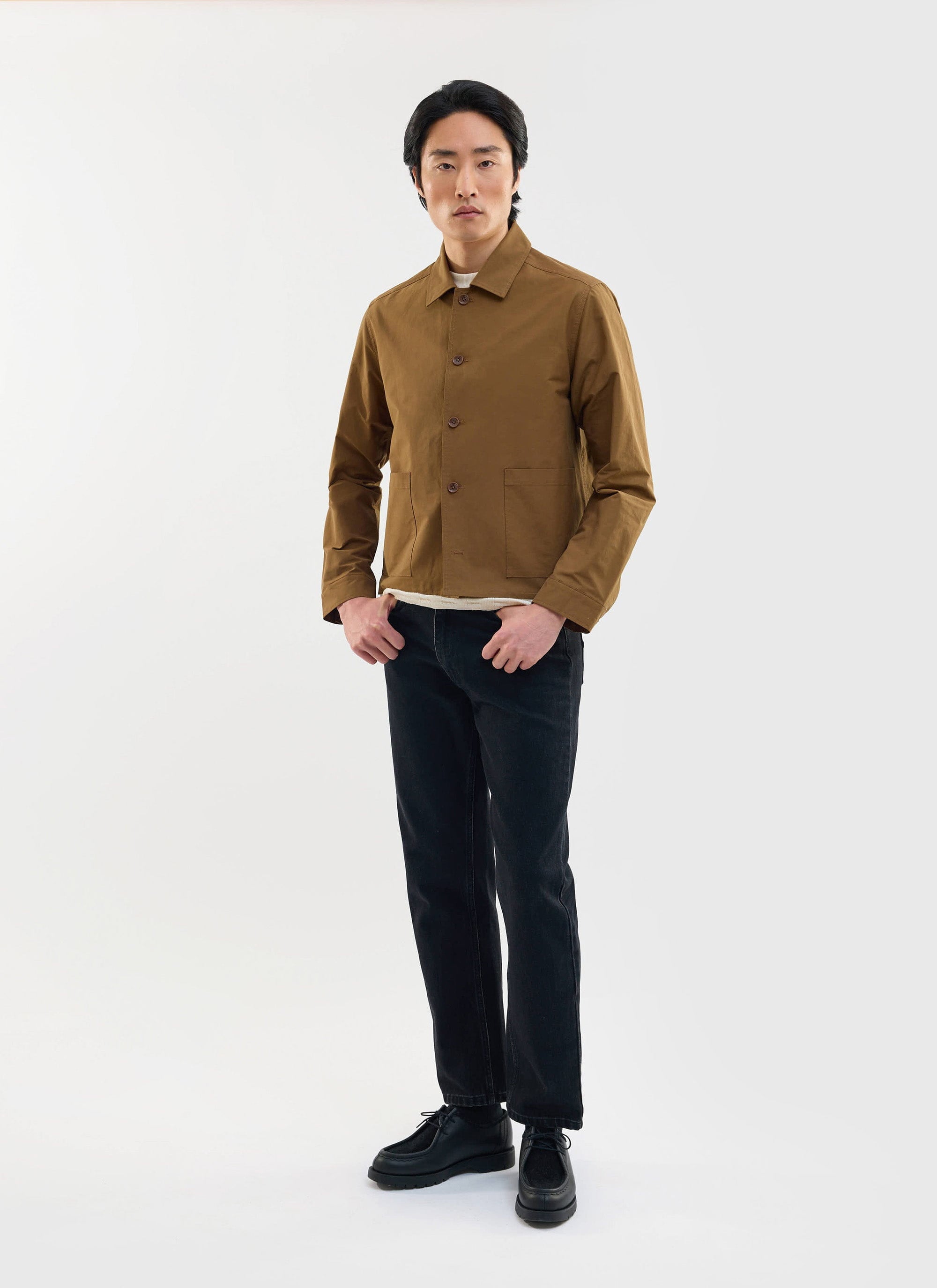 A man models the Percival Boxy Cropped Pocket Overshirt in brown, styled with dark jeans against a white background.
