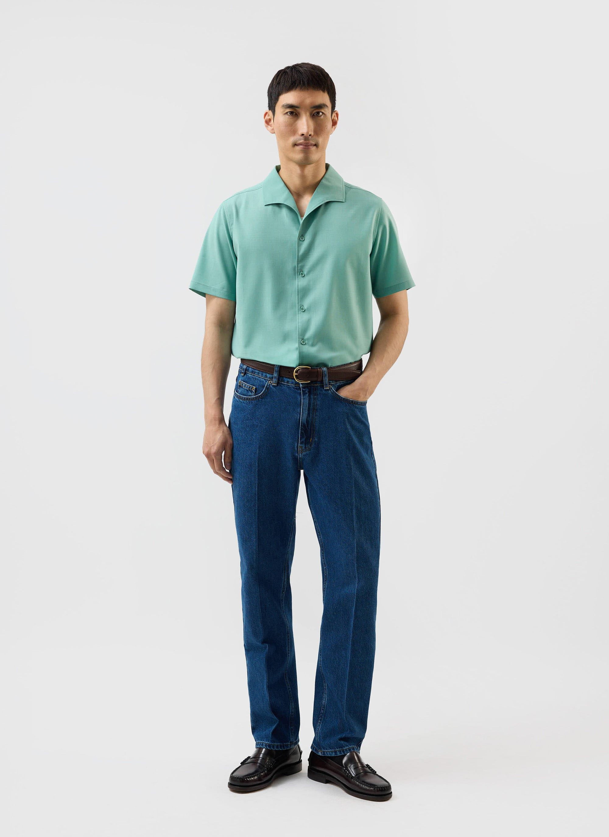 A man models the Percival x Warren Drape Cuban Shirt in mint green, styled with dark blue jeans and loafers.