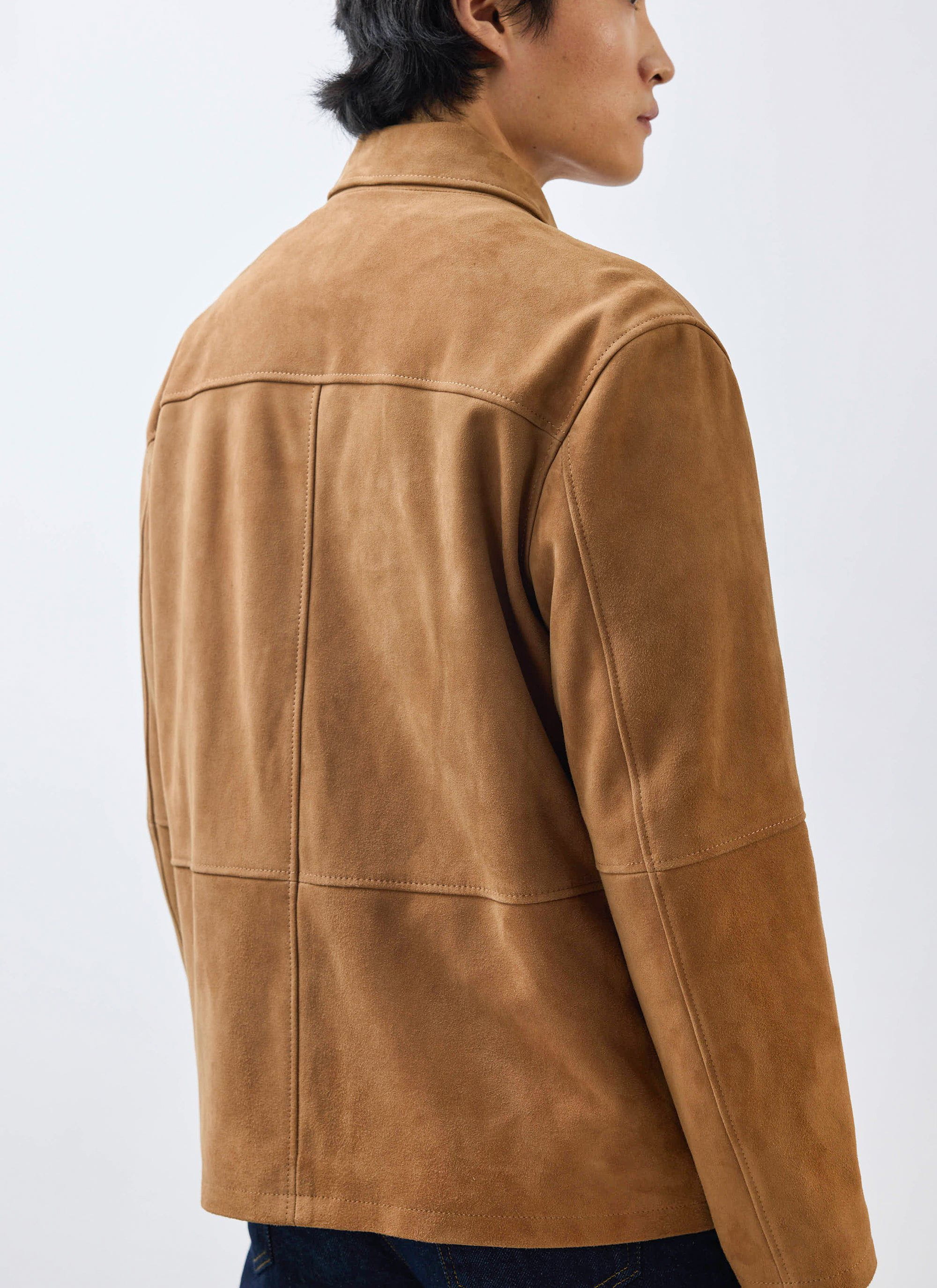 A model seen from behind wearing the Percival Afterward Suede Chore Jacket in tan, highlighting the panel detailing.