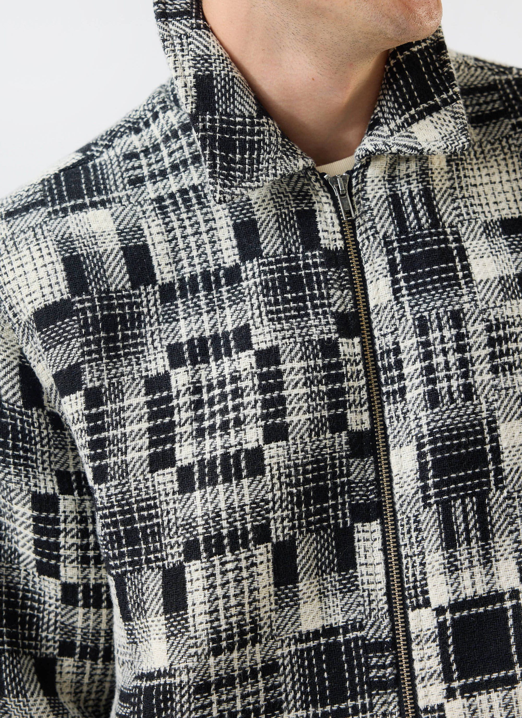 Close up of a model wearing the Percival Glossary Patchwork Jacket in grey, showing the woven twill texture and zip detail.