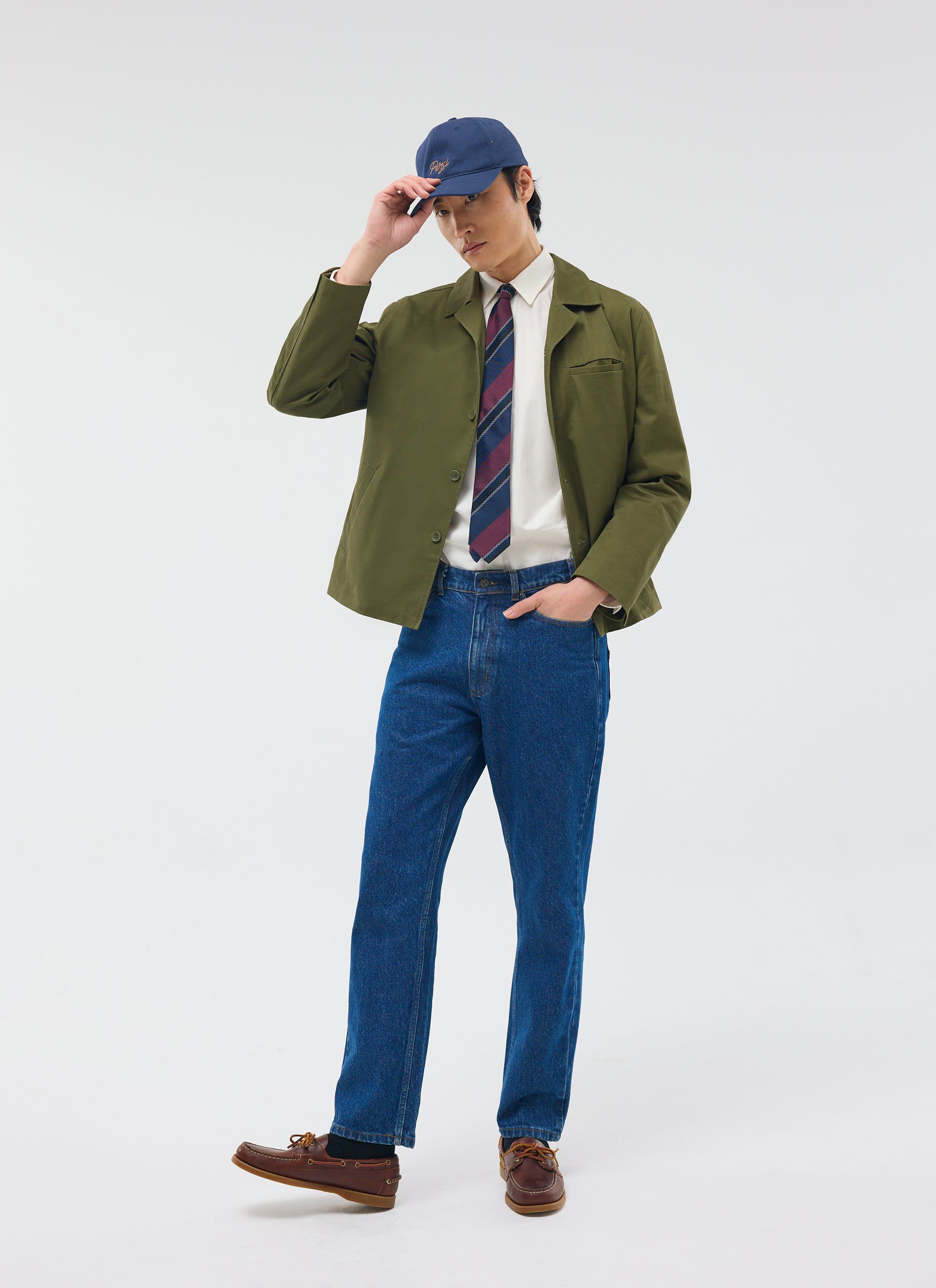 The Percival Casual Workwear Jacket in khaki, styled on a model with a shirt, tie, blue jeans and a baseball cap.
