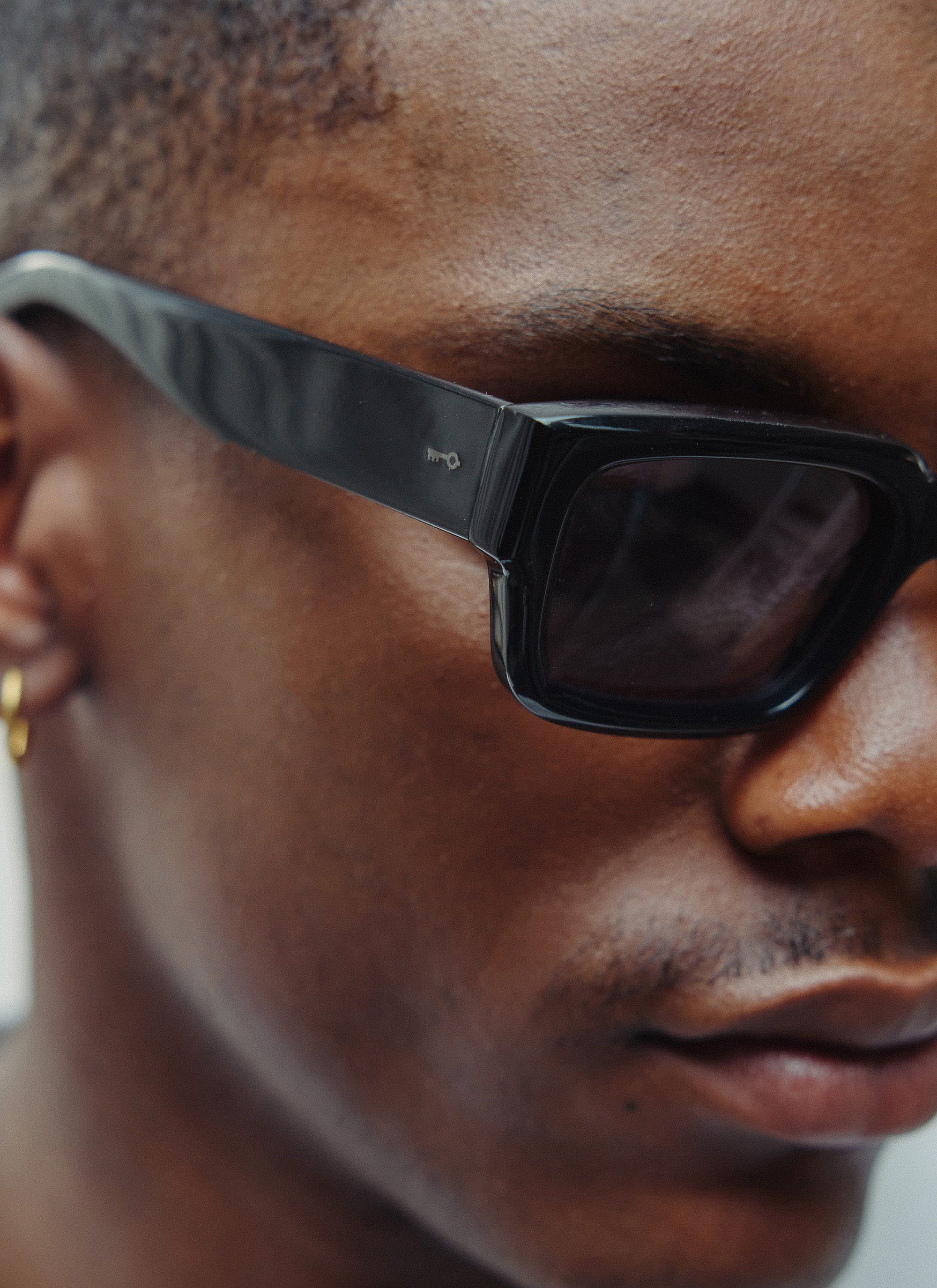 Close up of a model wearing the Percival P002-E2 black sunglasses, showing the subtle key logo on the arm.