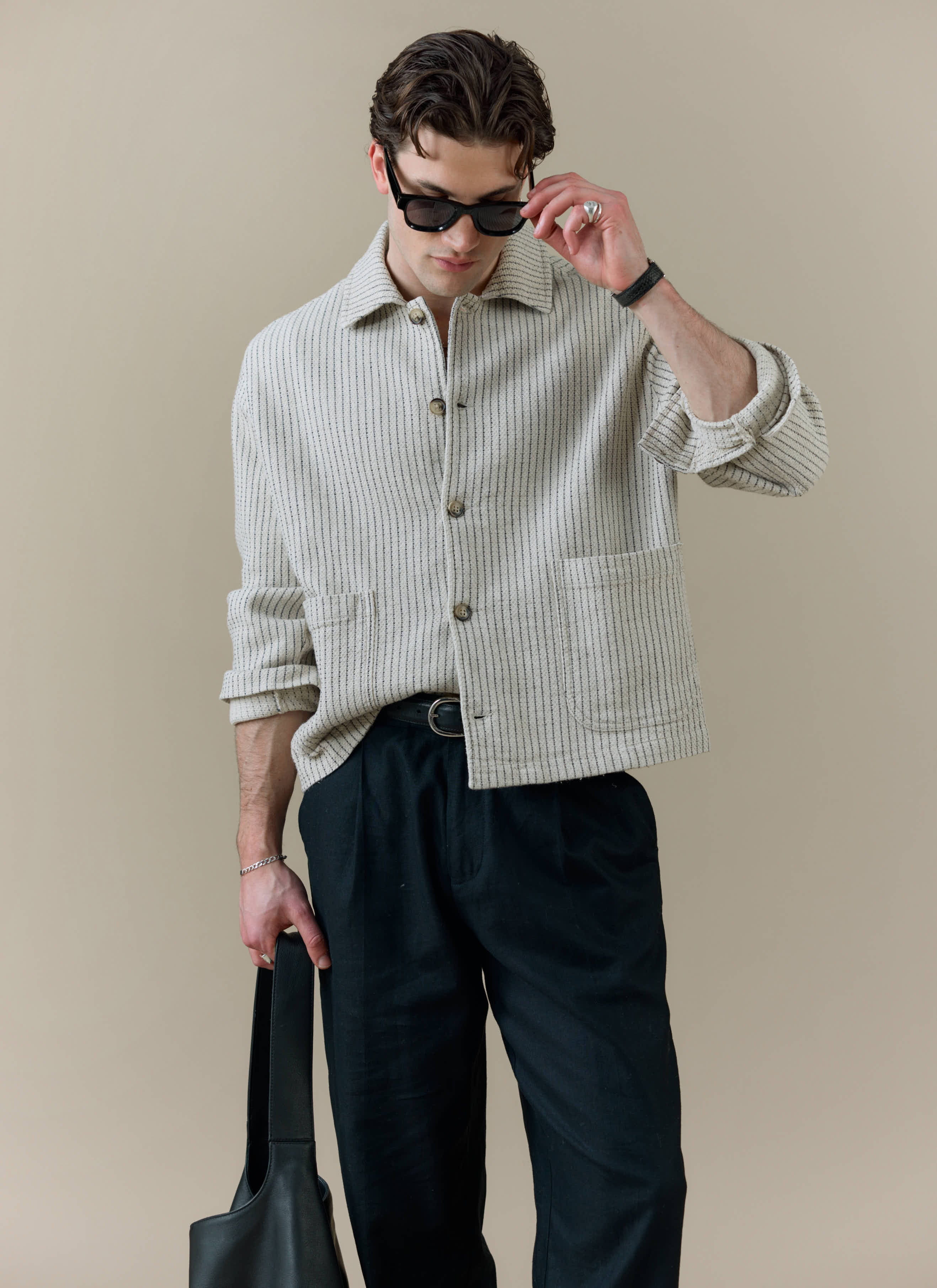A model wearing the Percival Sorrento Boxy Overshirt in cream linen with vertical texture and black trousers.
