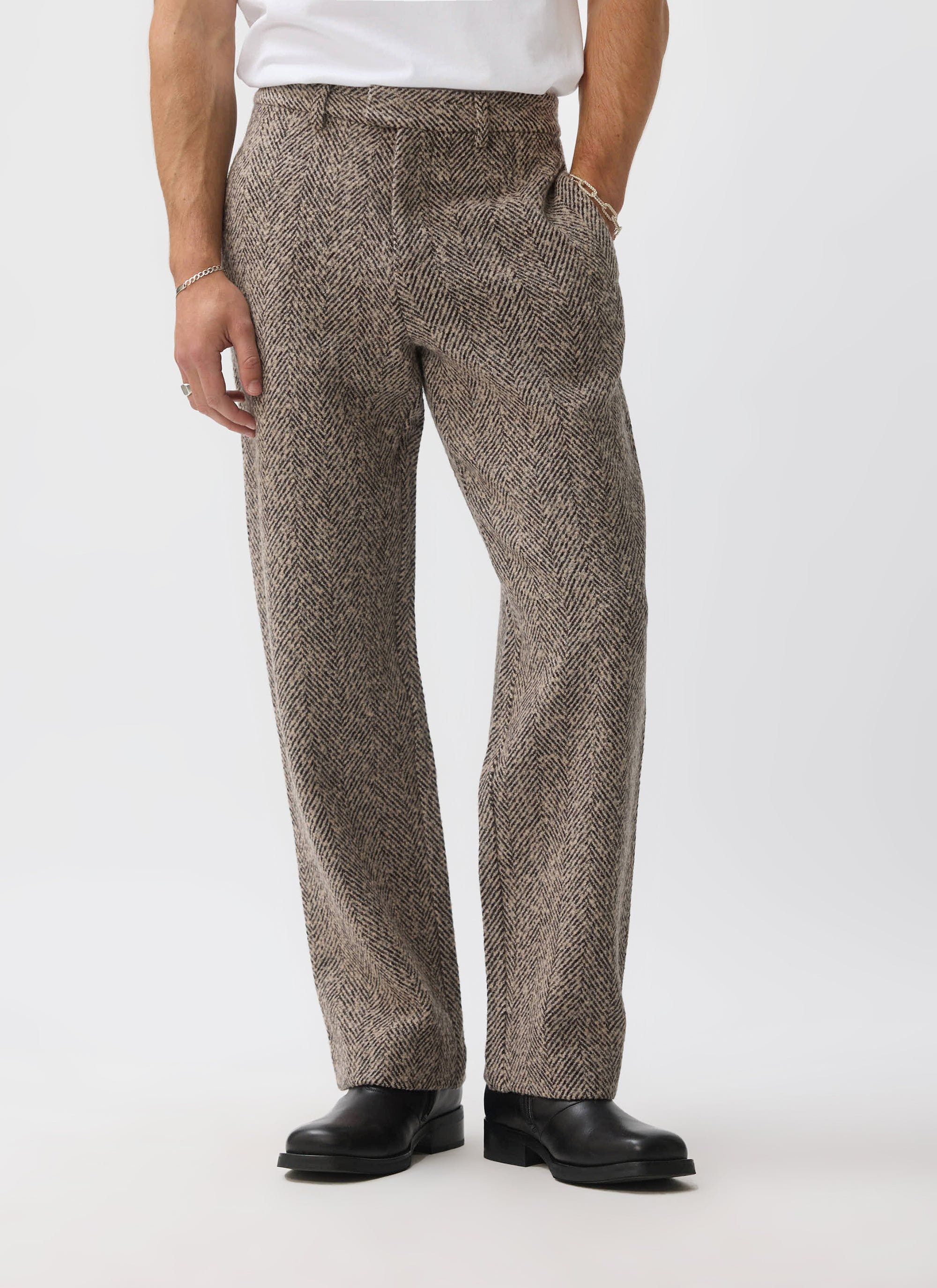 A man models the ecru wool Herringbone Trousers from Percival, paired with a white t-shirt and black boots.