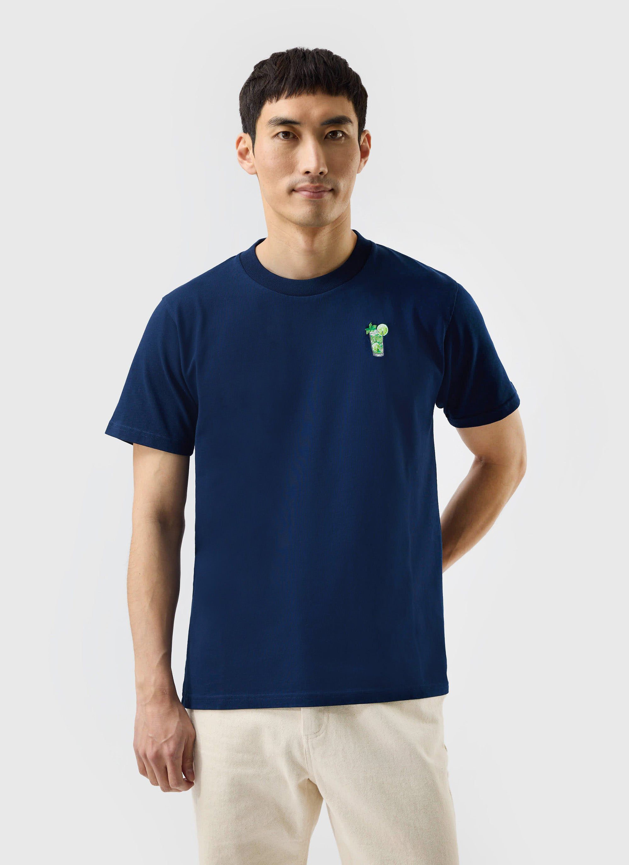 A model wears the navy organic cotton Mojito T-shirt from Percival, featuring a small cocktail embroidery on the chest.