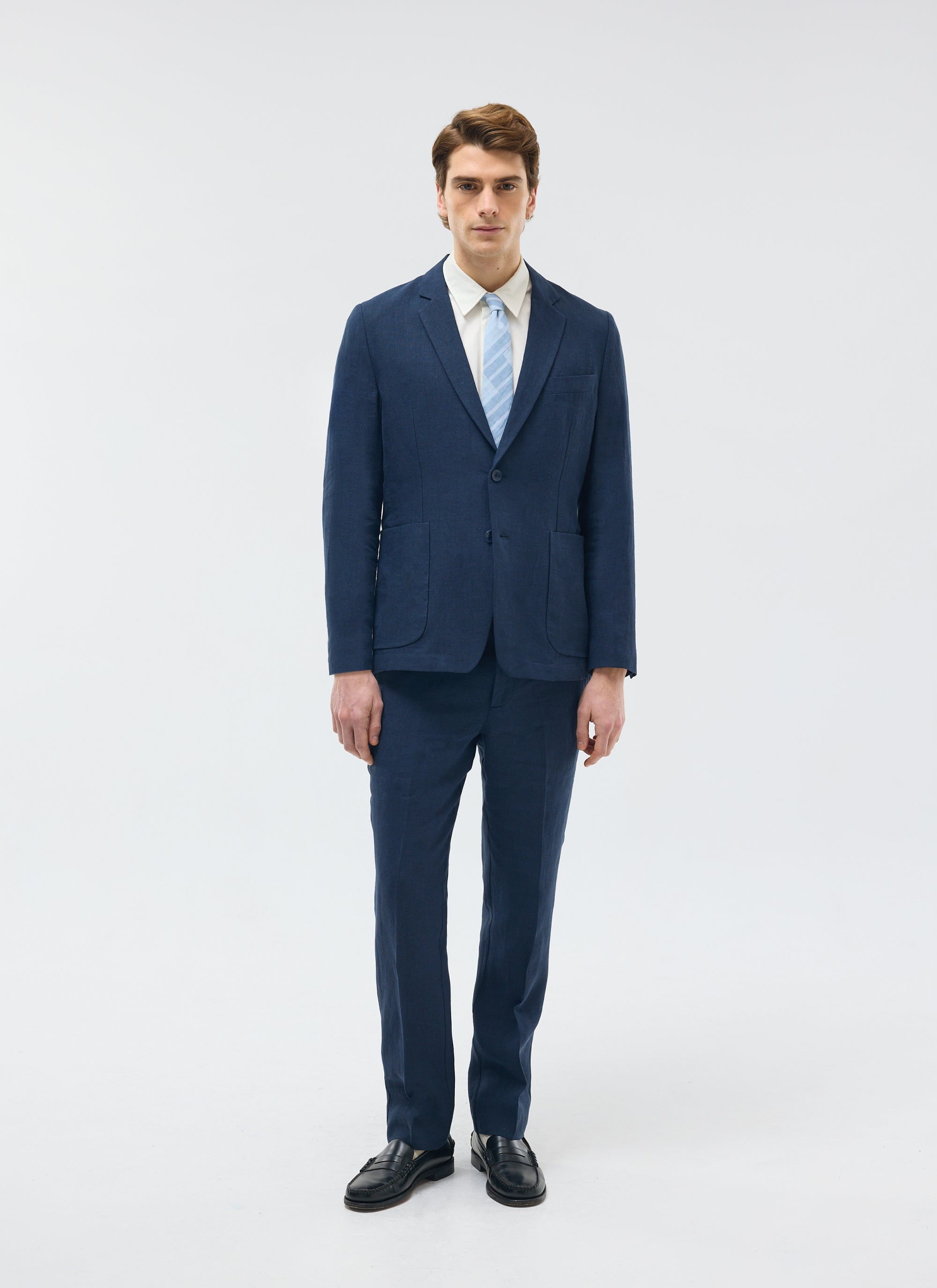 A model wears the Percival navy tailored linen trousers and matching blazer with a white shirt and light blue tie.