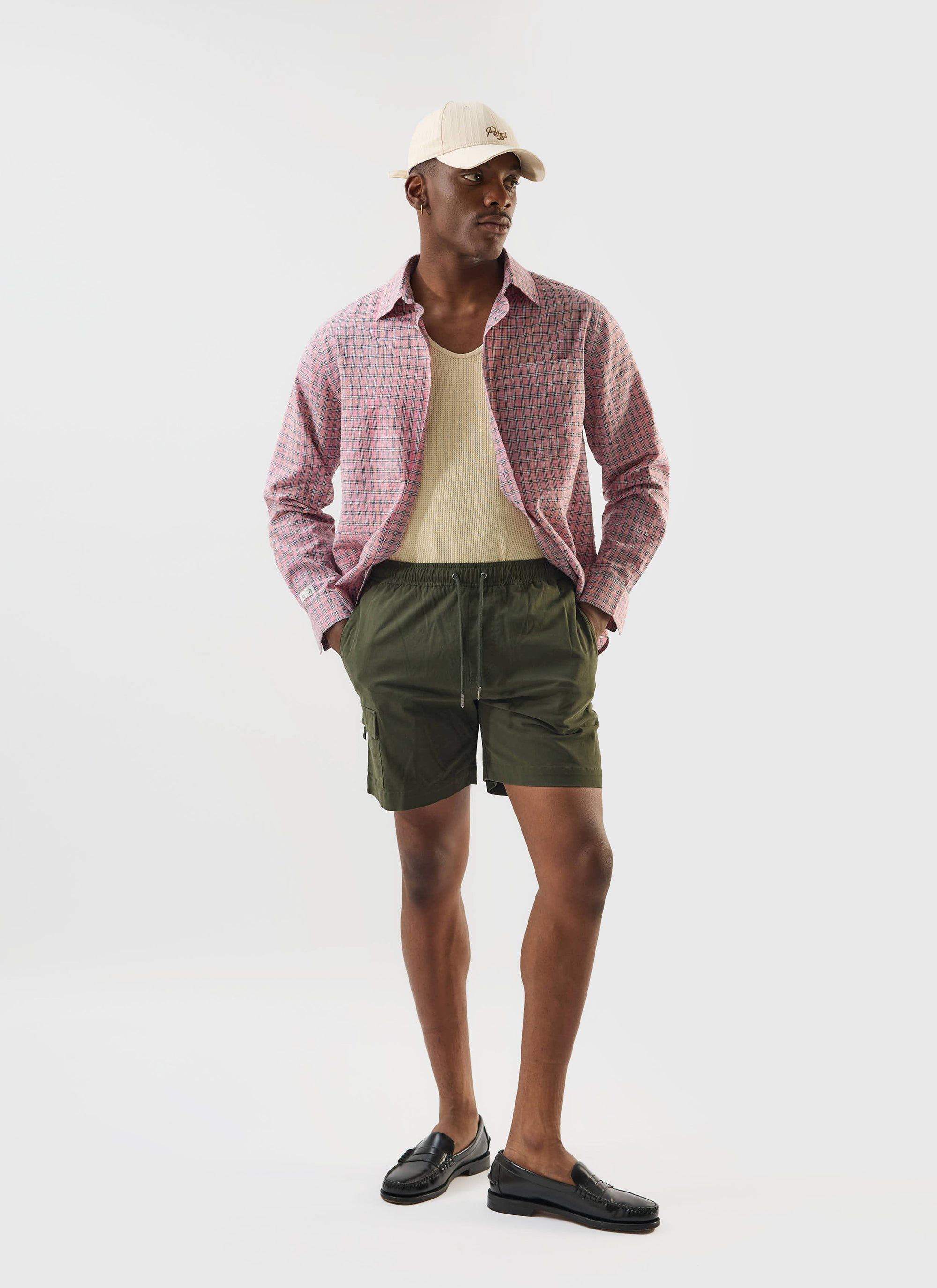 A model wears the Percival Cotton Waffle Vest in ecru, layered under a pink checked shirt with olive green shorts.