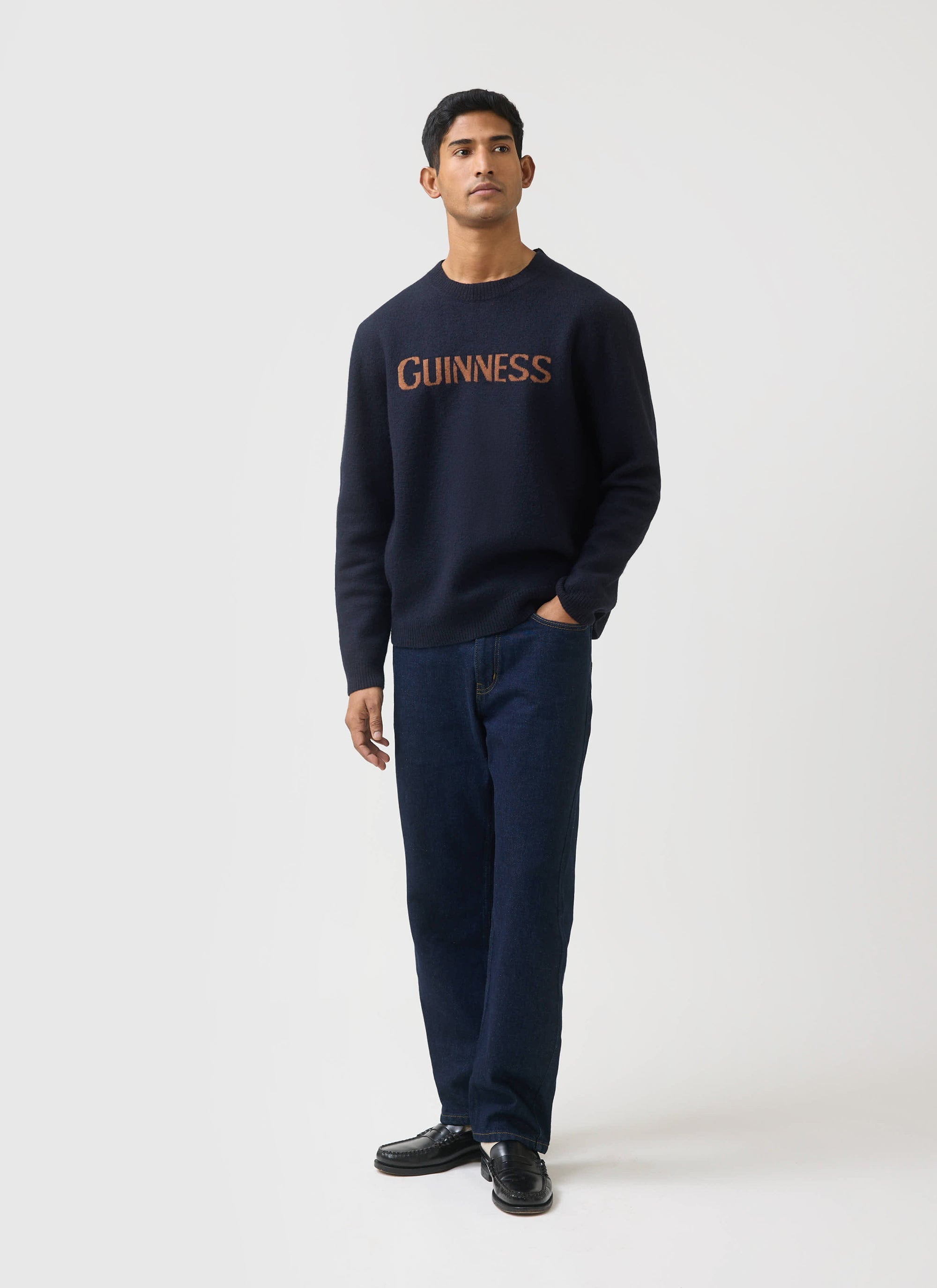 A model wears the navy Guinness x Percival merino wool jumper, styled with dark jeans and black loafers.