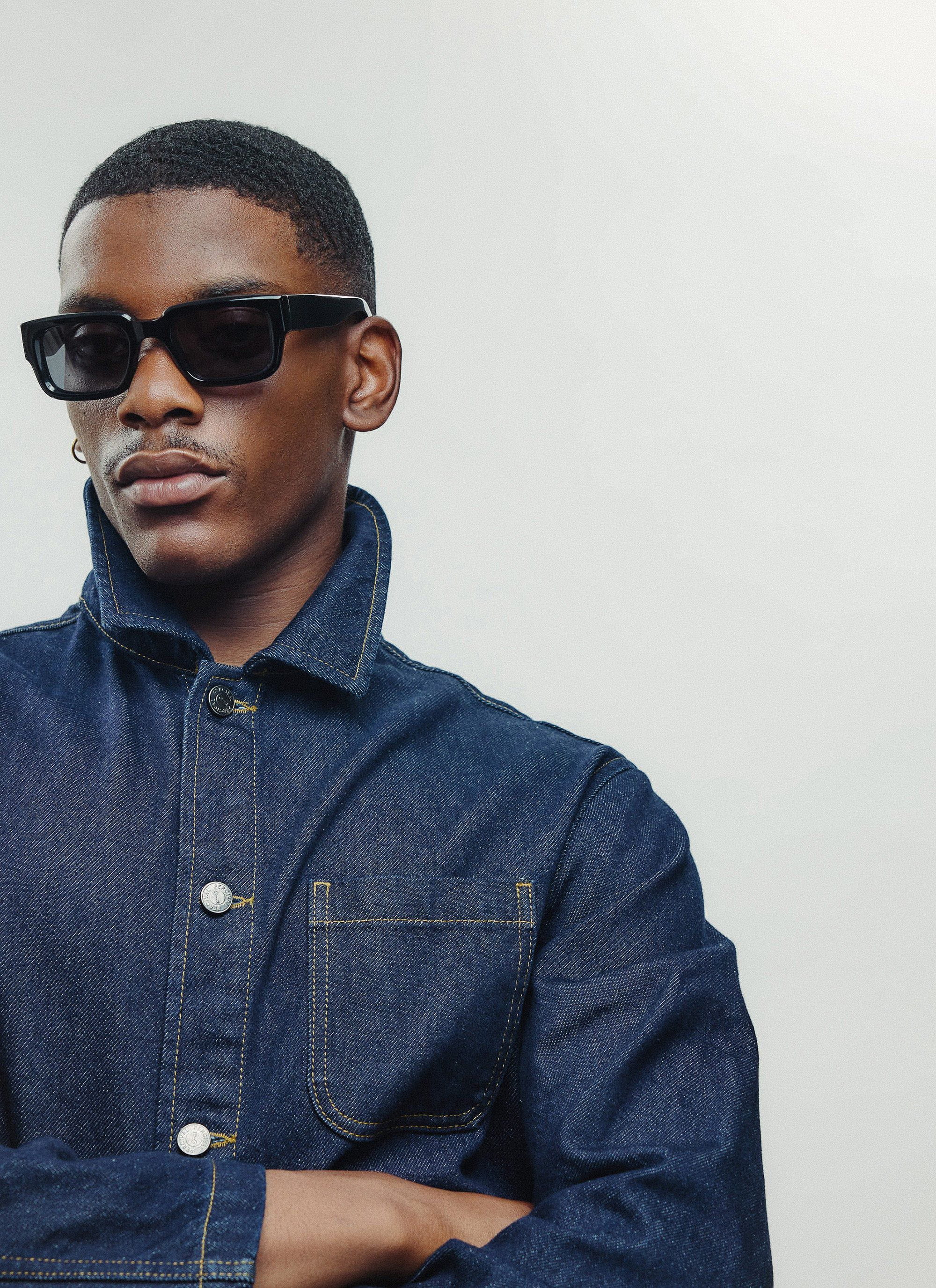 A model wearing a dark denim jacket and the classic P002-E2 black sunglasses from Percival.