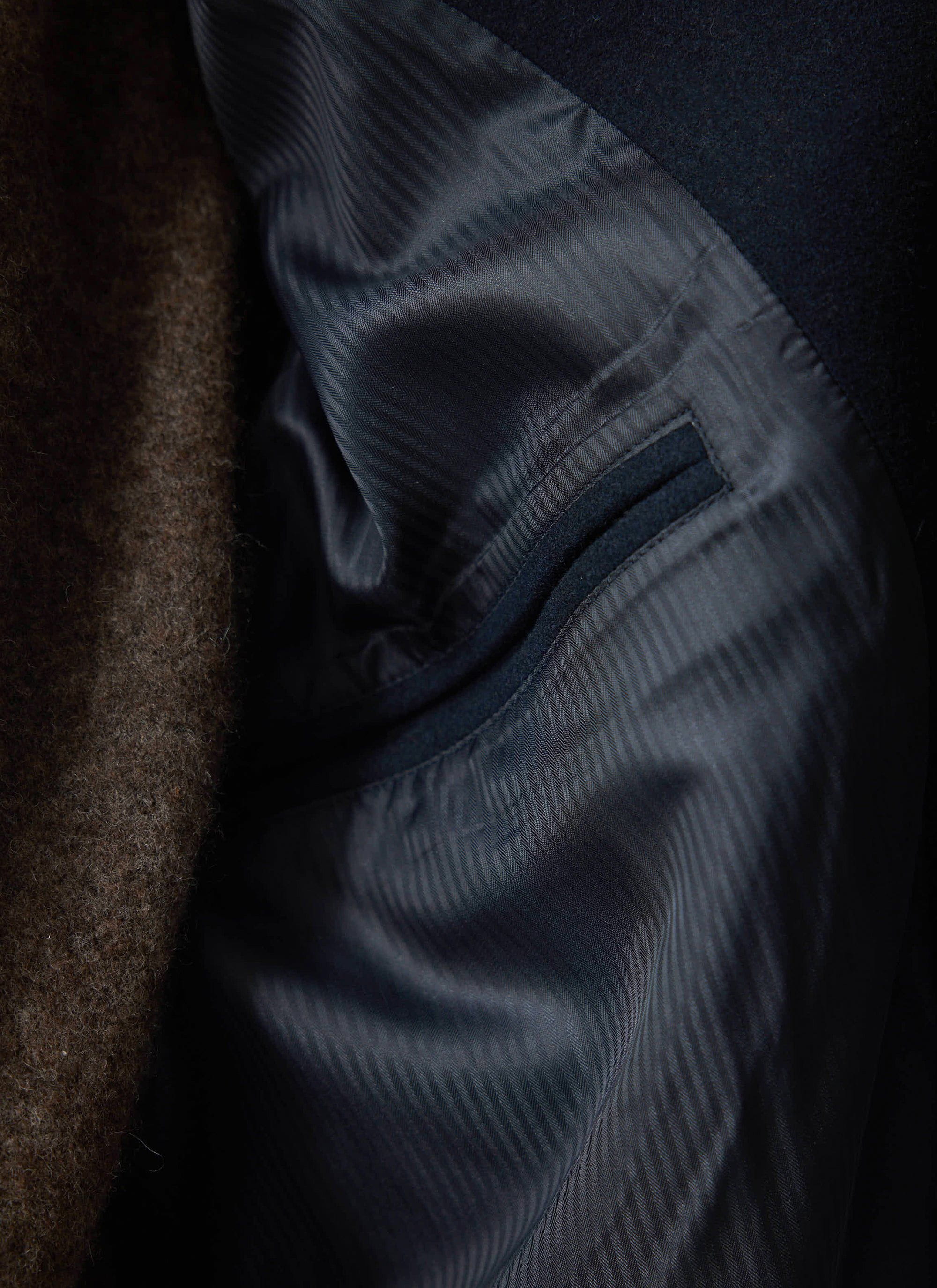 A close-up of the patterned interior lining and internal pocket of the navy wool car coat by Percival.
