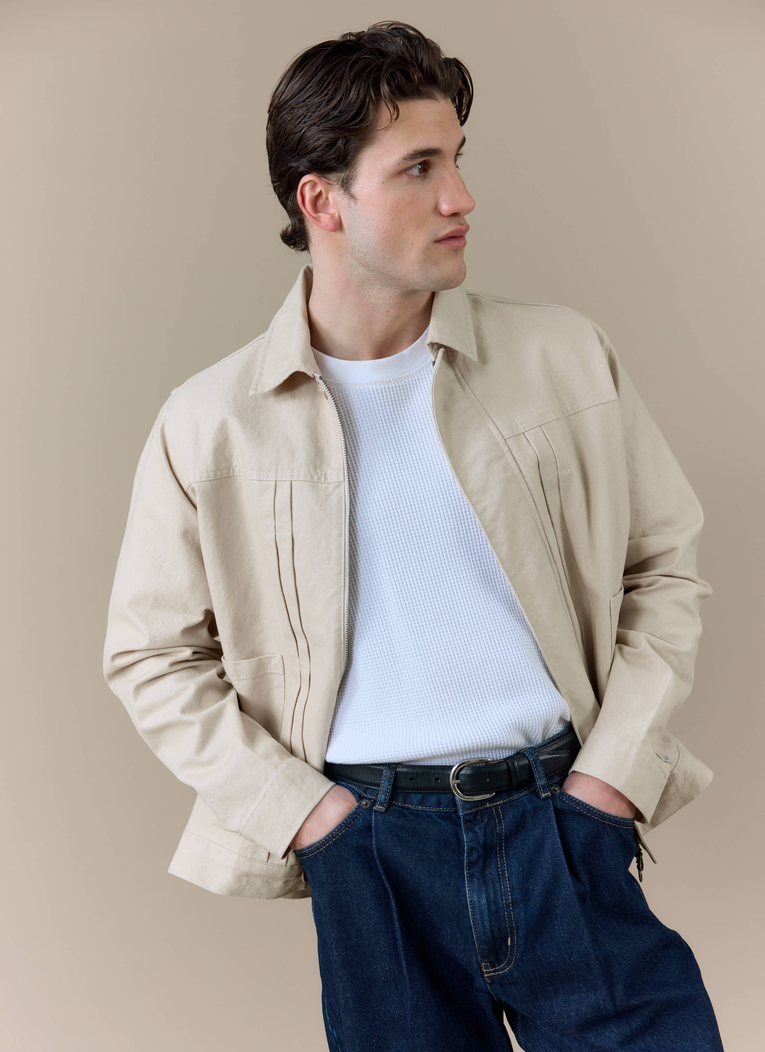 A model wearing the cream cotton Ernst Jacket from Percival, featuring twin pleat detailing and a zip front.