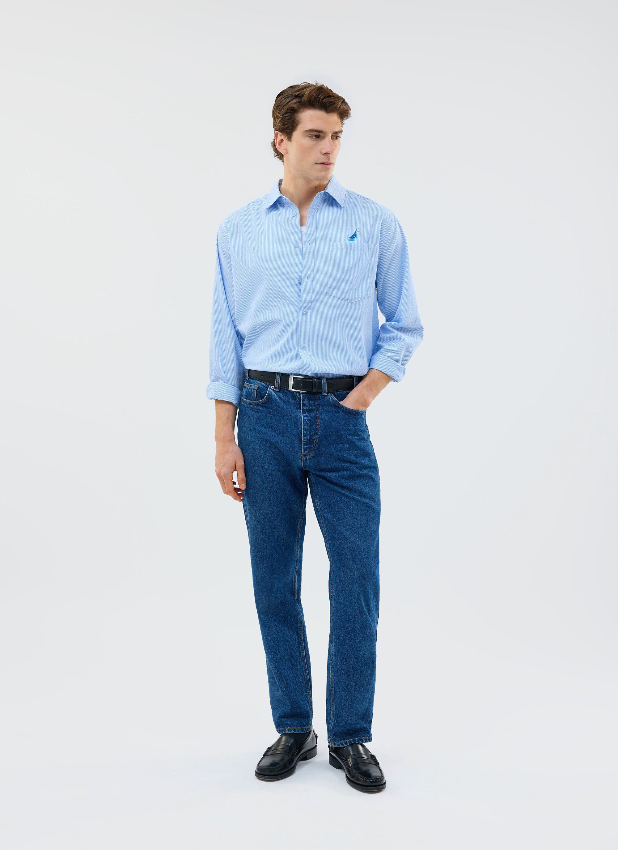 A model wears the Percival Yacht Stripe Oversized Shirt in blue, styled with dark wash jeans and black loafers.