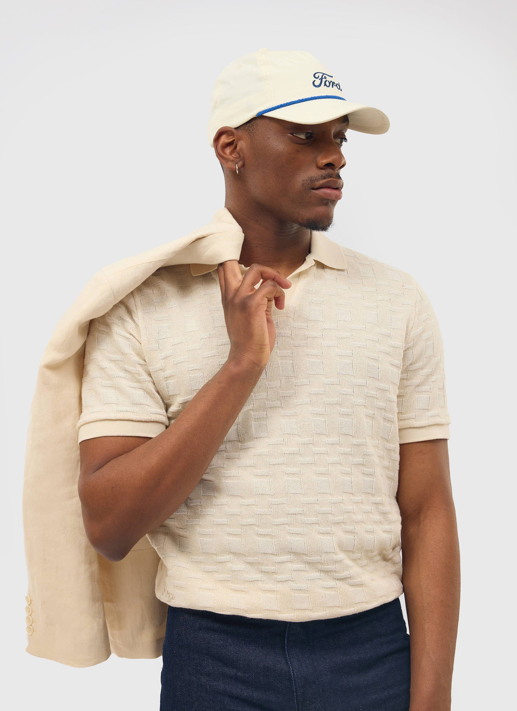 A model wears the Percival Deck Negroni Knitted Shirt in ecru, with a matching jacket slung over his shoulder.