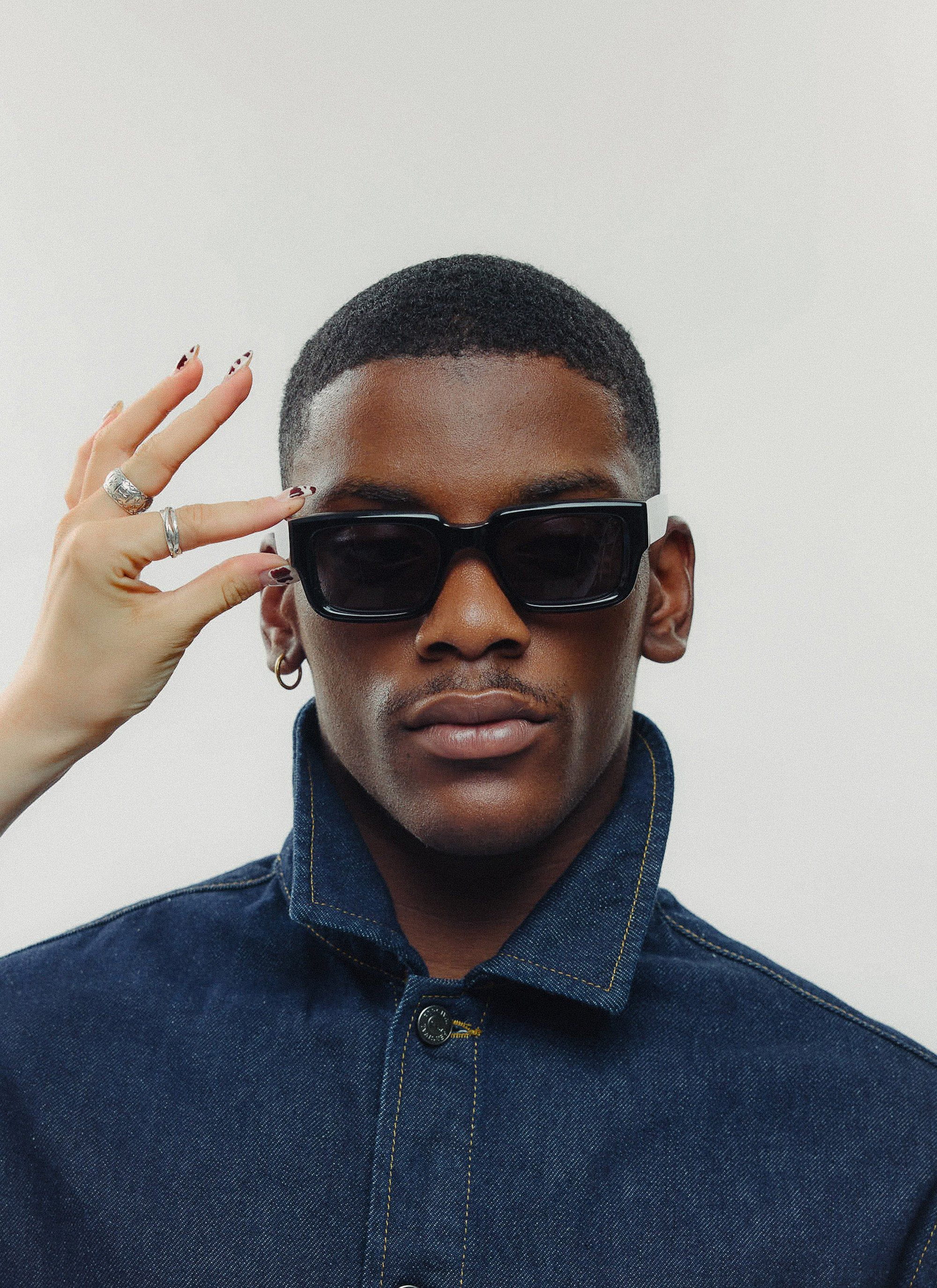 A close-up of a model wearing the P002-E2 black sunglasses from Percival, with a woman's hand adjusting the frames.