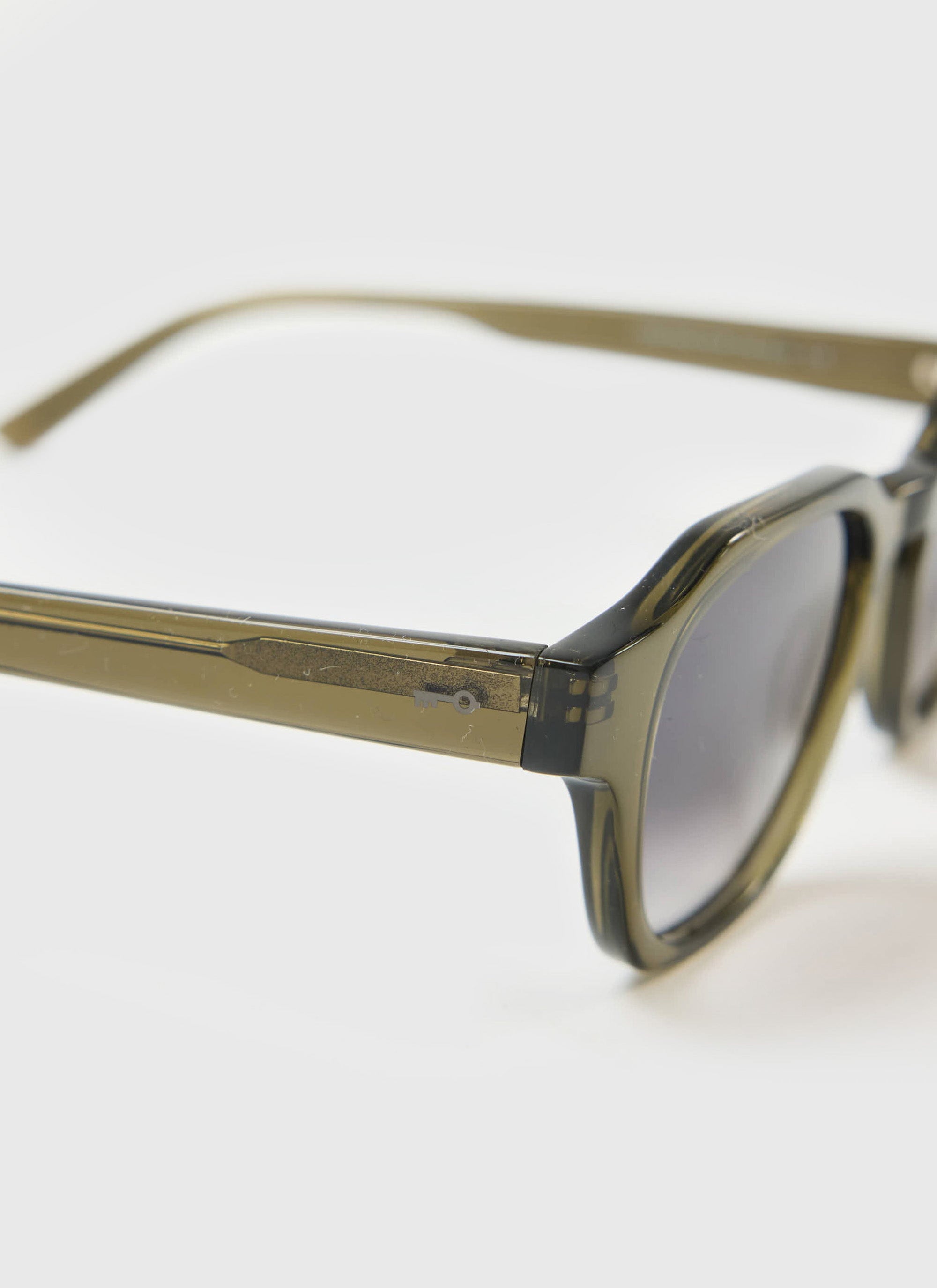 A close-up of the Percival olive green sunglasses, focusing on the bioacetate frame and subtle key logo on the temple.