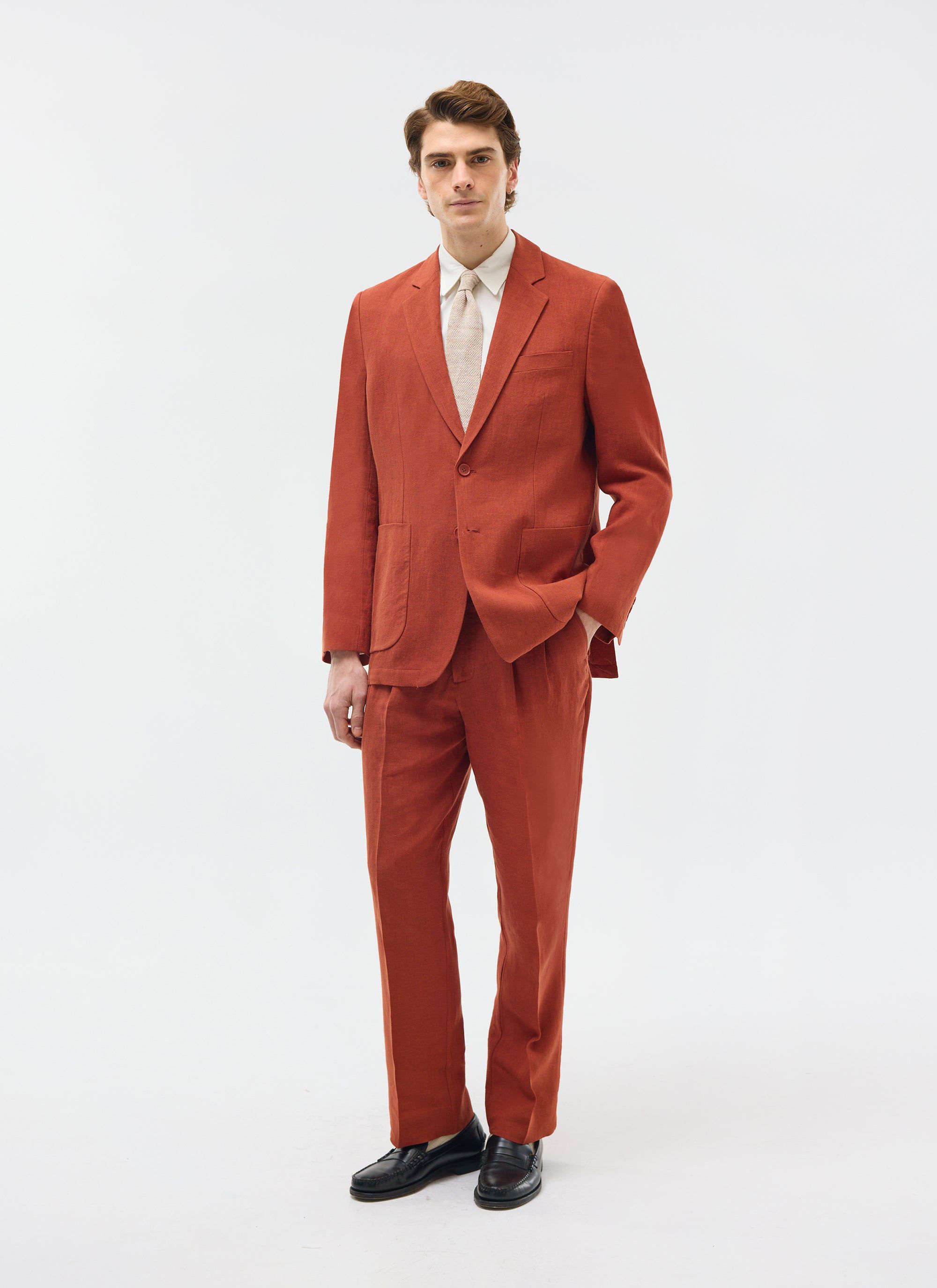 Model wearing Percival rust linen pleated trousers with matching blazer, shirt, tie and black loafers on a white background